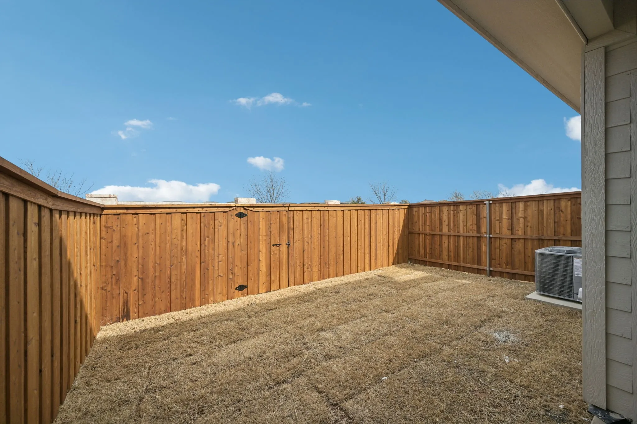 Enclosed backyard space featuring wood panel fencing, dry grass landscaping, and a visible HVAC unit
