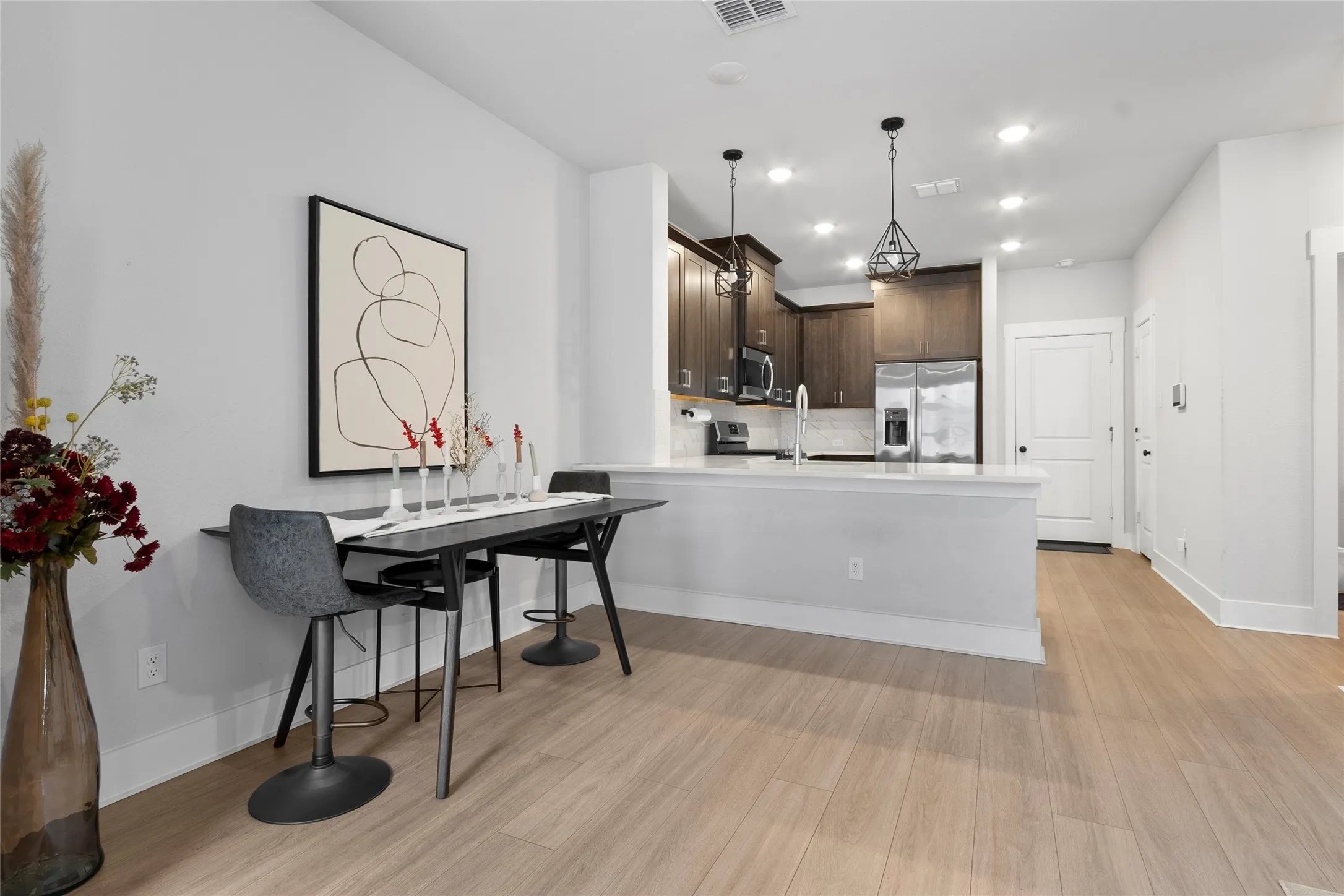 Open-concept kitchen and dining area featuring light wood-finish flooring, dark wood cabinetry, stainless steel appliances, a kitchen island with a white countertop, and recessed lighting