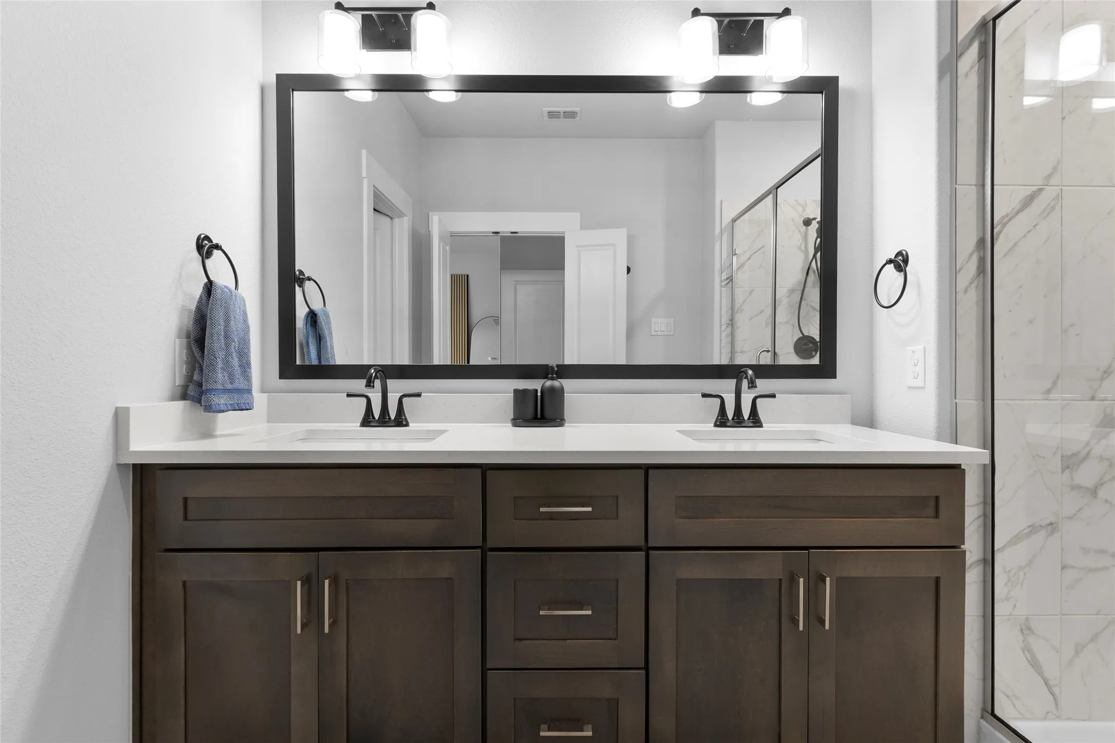 Dual vanity featuring wood-finish cabinetry, white countertops, and matte black fixtures