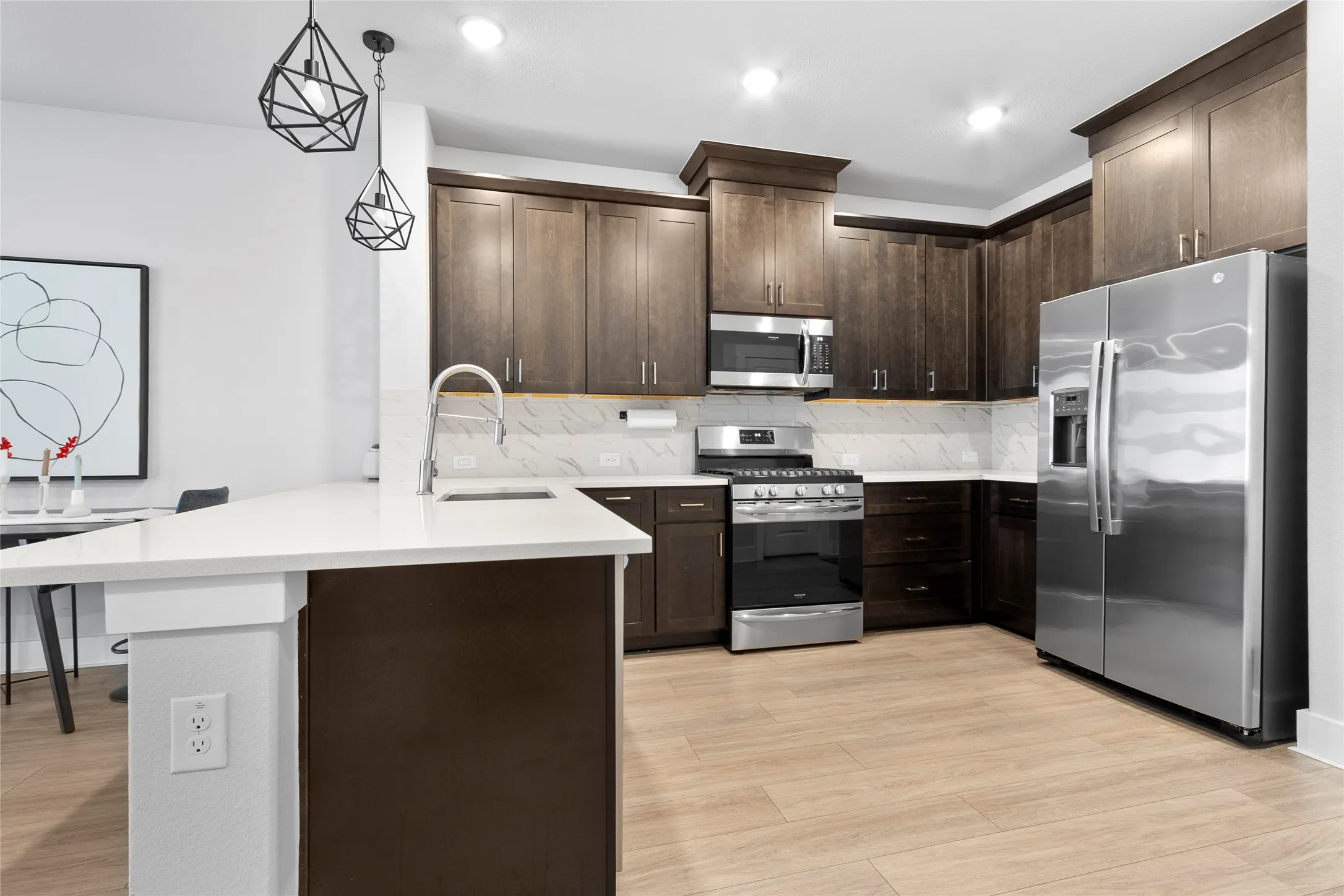 Modern kitchen featuring light wood-finish flooring, dark wood cabinetry, white countertops, and a white tile backsplash