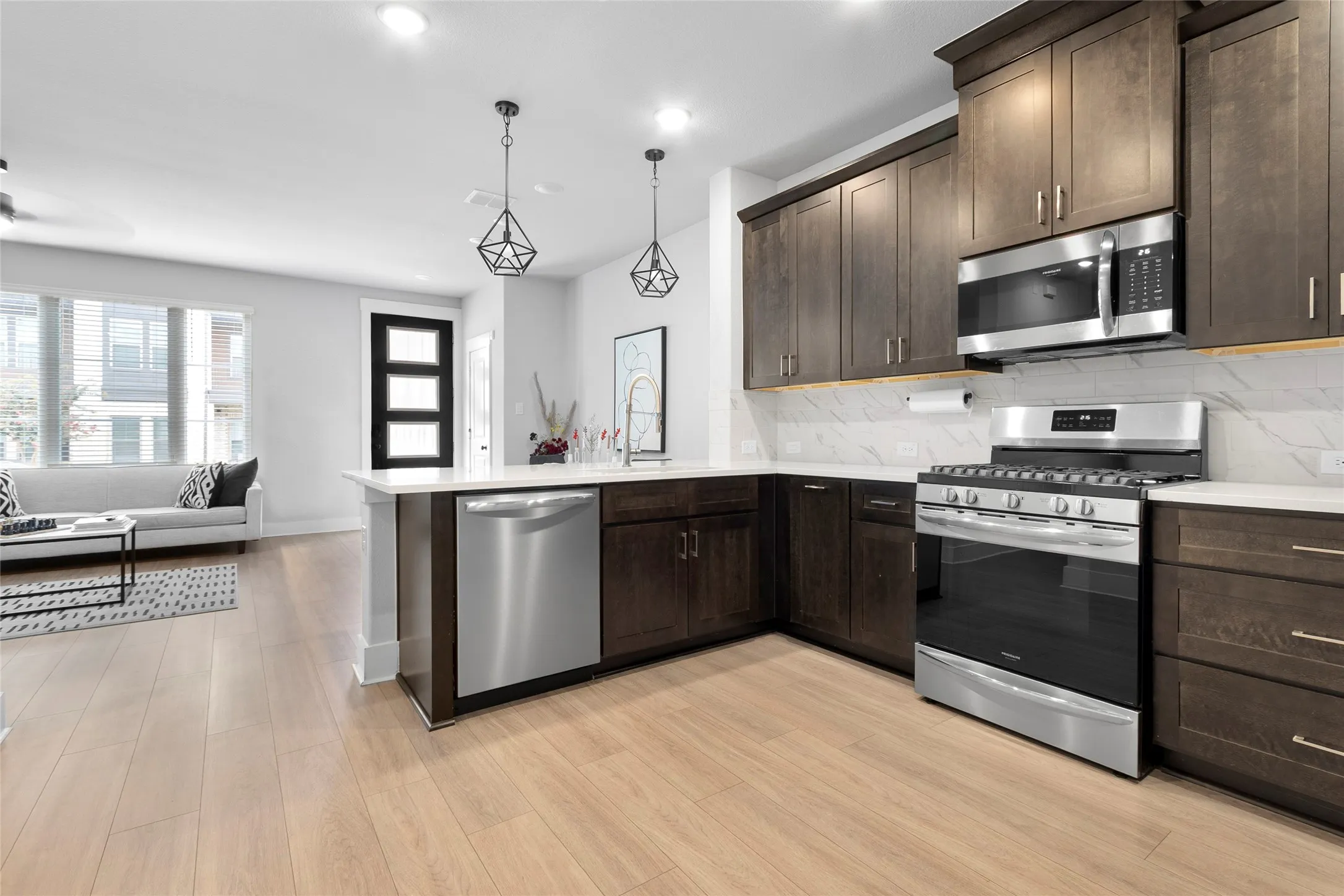 Modern kitchen featuring dark wood cabinetry, stainless steel appliances, a white tile backsplash, and light wood-finish flooring