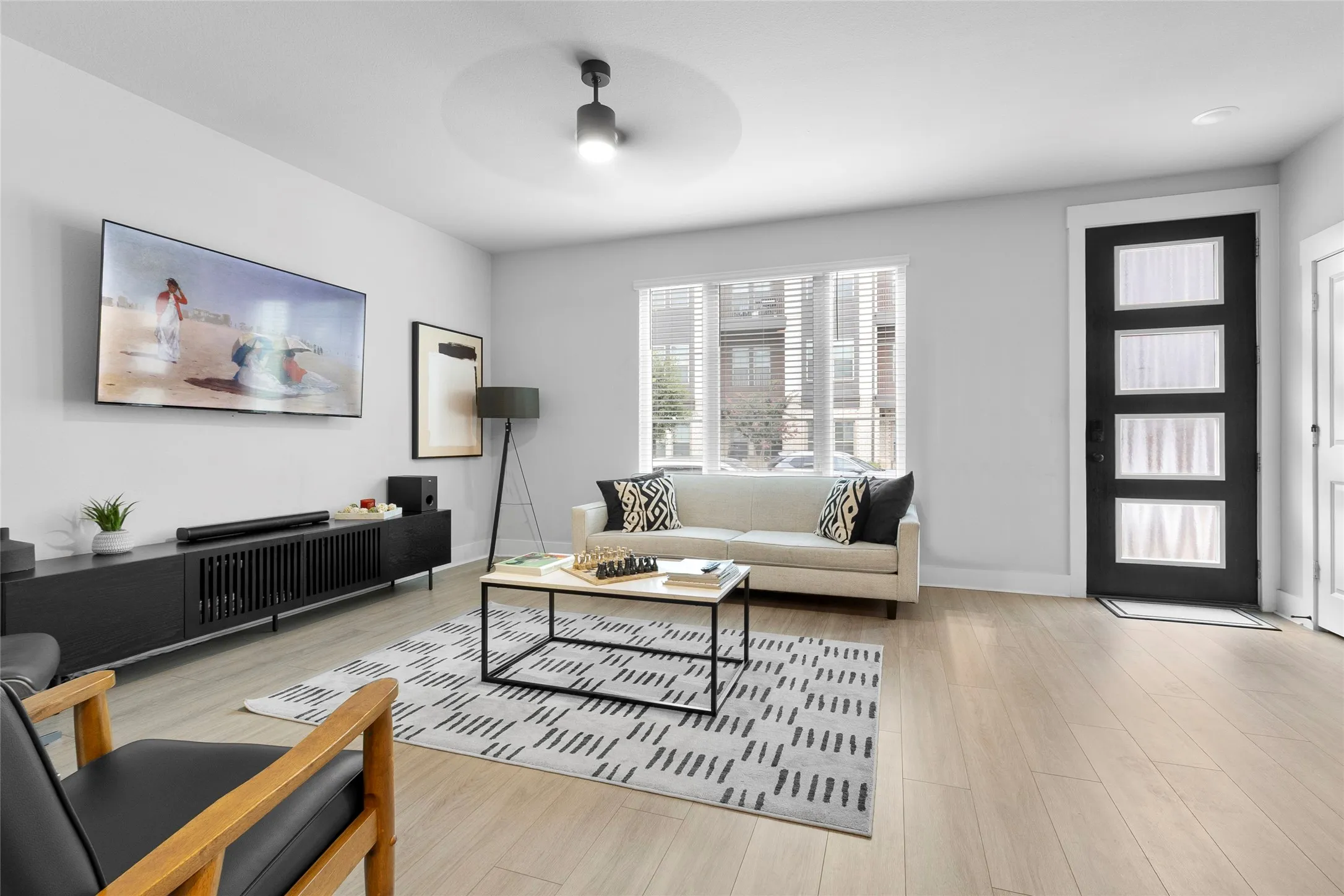 Living area featuring wood-finish flooring, a modern black entry door with frosted glass panels, and a ceiling fan with integrated lighting