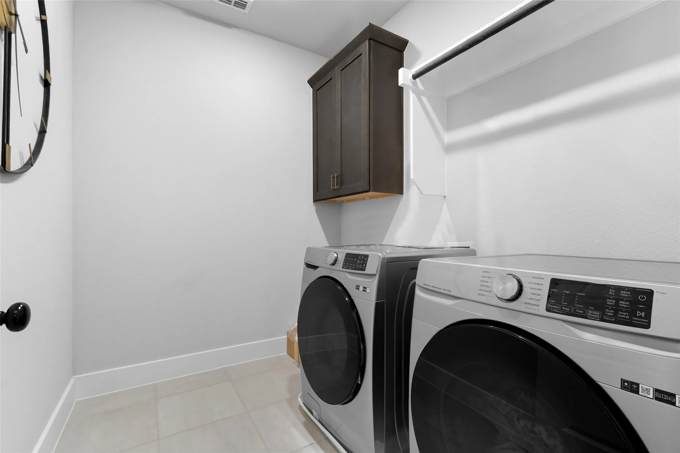 Dedicated laundry space featuring a built-in dark wood-finish cabinet, a clothes hanging rod, and light-toned tile flooring