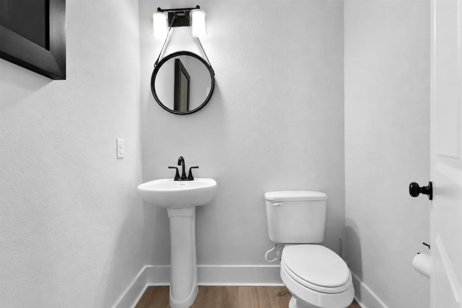Downstairs Powder Rooom with Pedestal sink with matte black faucet, round mirror, and complementary wall-mounted light fixture