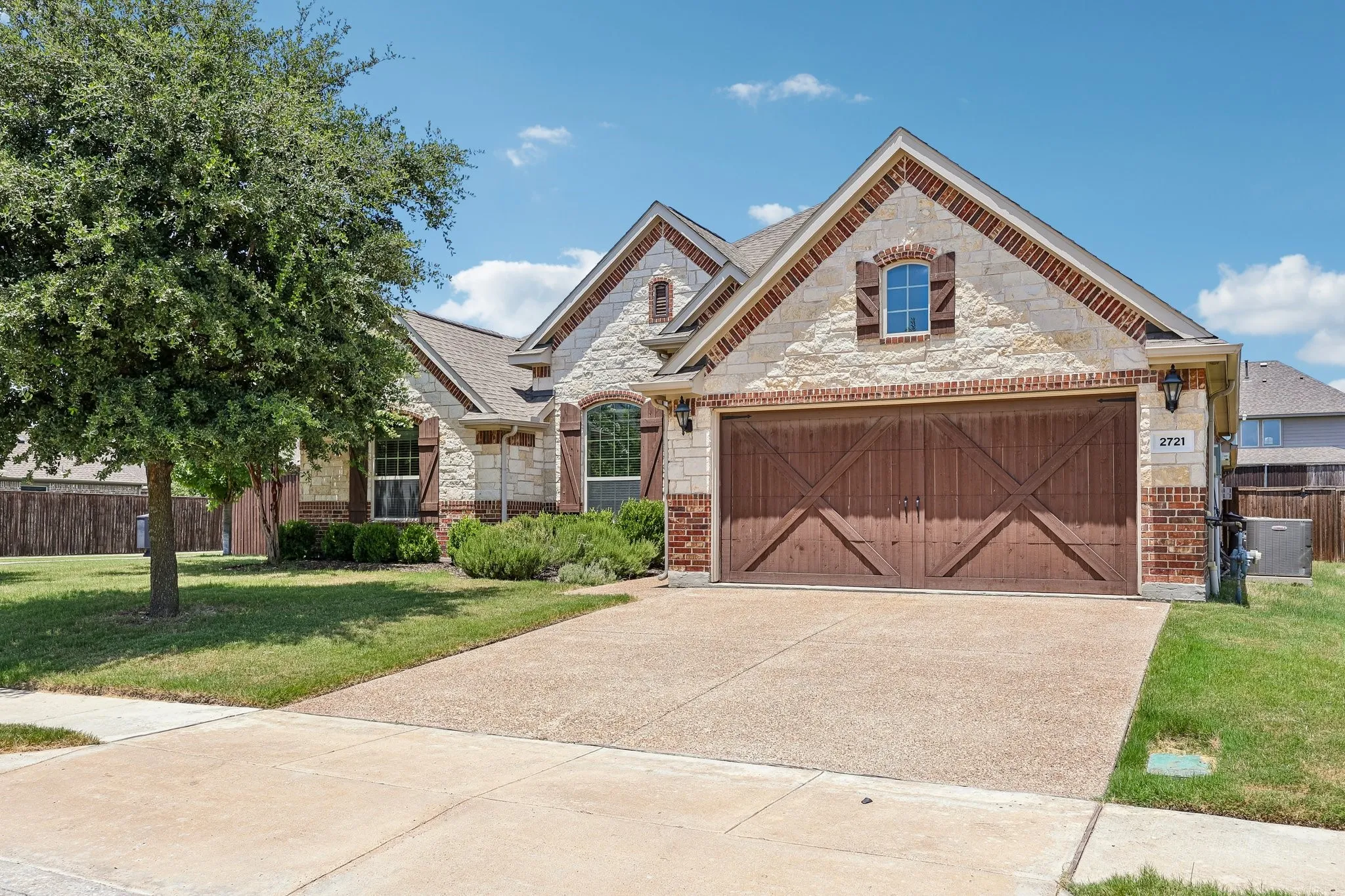 Stone and brick veneer exterior with a two-car garage featuring decorative wood doors
