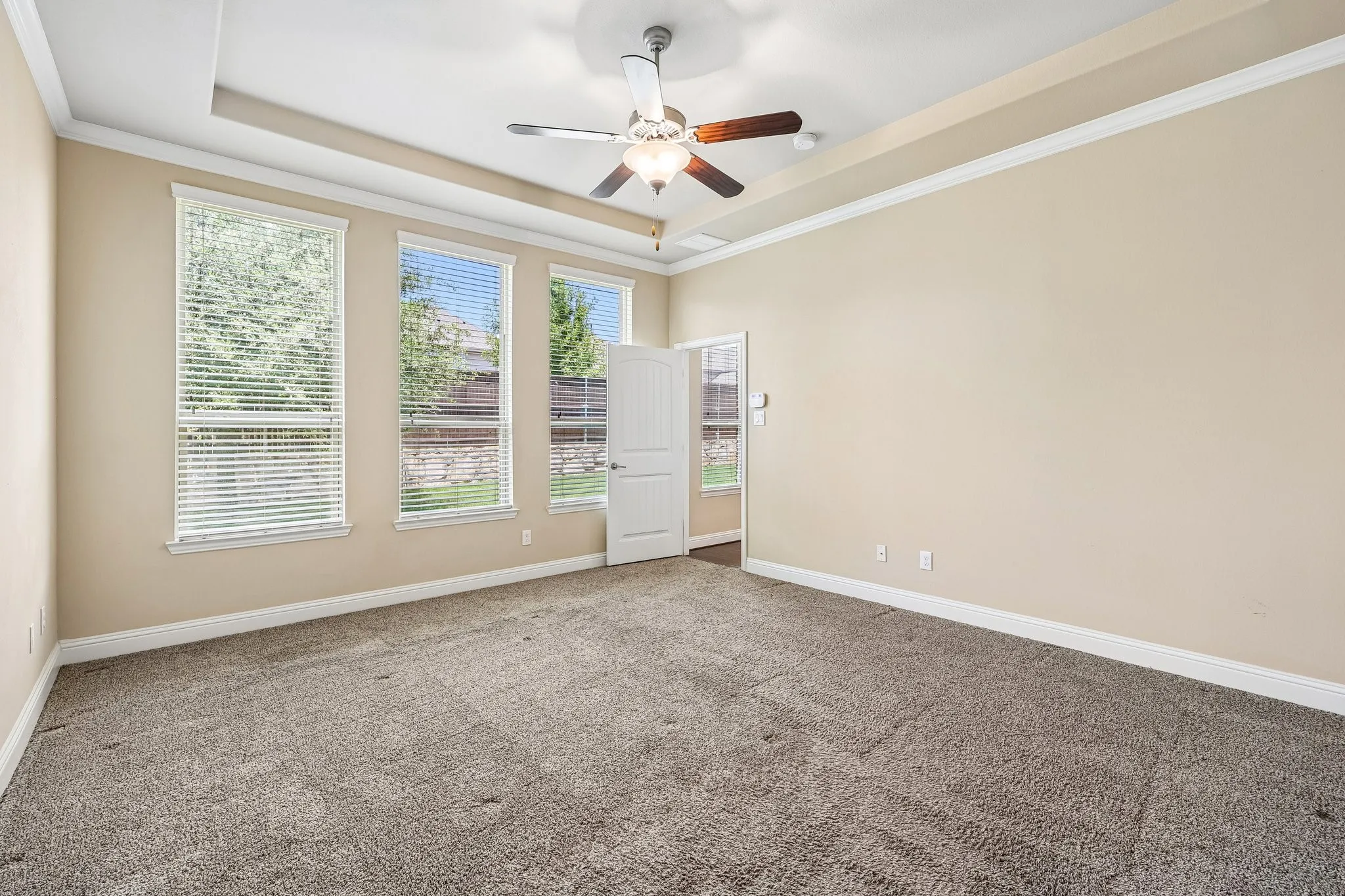 Spacious room featuring neutral carpeting, light-toned walls, and a tray ceiling with a ceiling fan