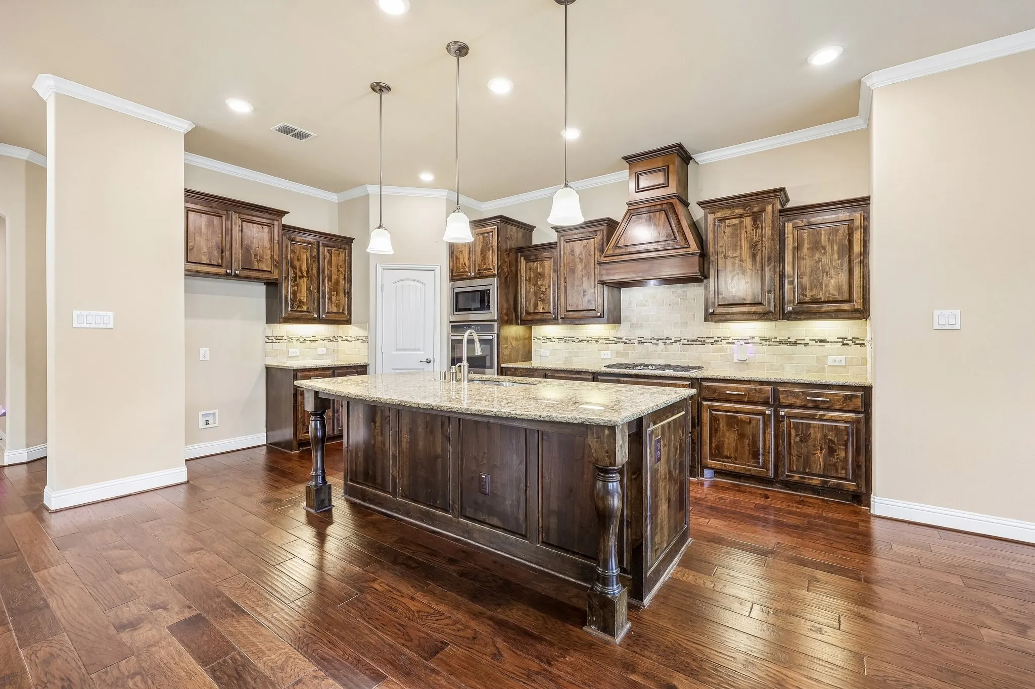 Spacious kitchen featuring an expansive center island with a granite countertop, rich wood cabinetry, stainless steel appliances, and wood-finish flooring