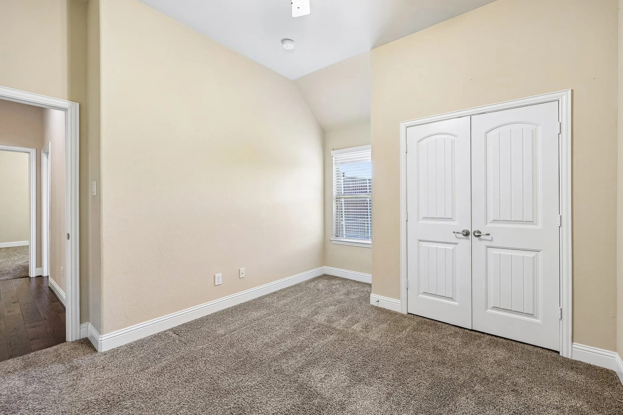 Carpeted room featuring a single window with blinds, white trim, and a double-door closet with arch-top panels
