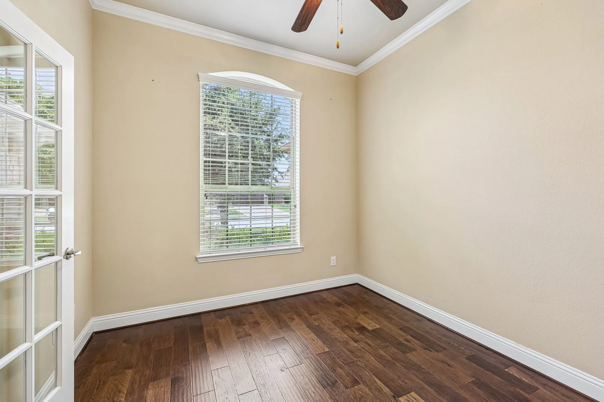 Room featuring hardwood flooring, an arched window with blinds, French doors, crown molding, and a ceiling fan
