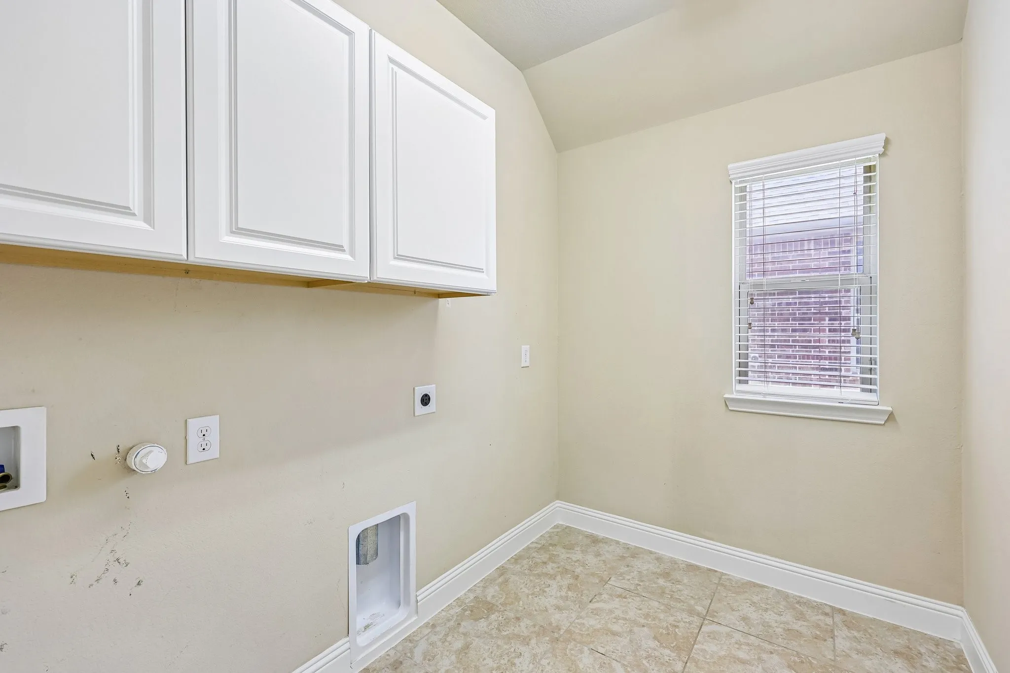 Laundry area with white shaker-style cabinetry, tile flooring, and a window featuring blinds