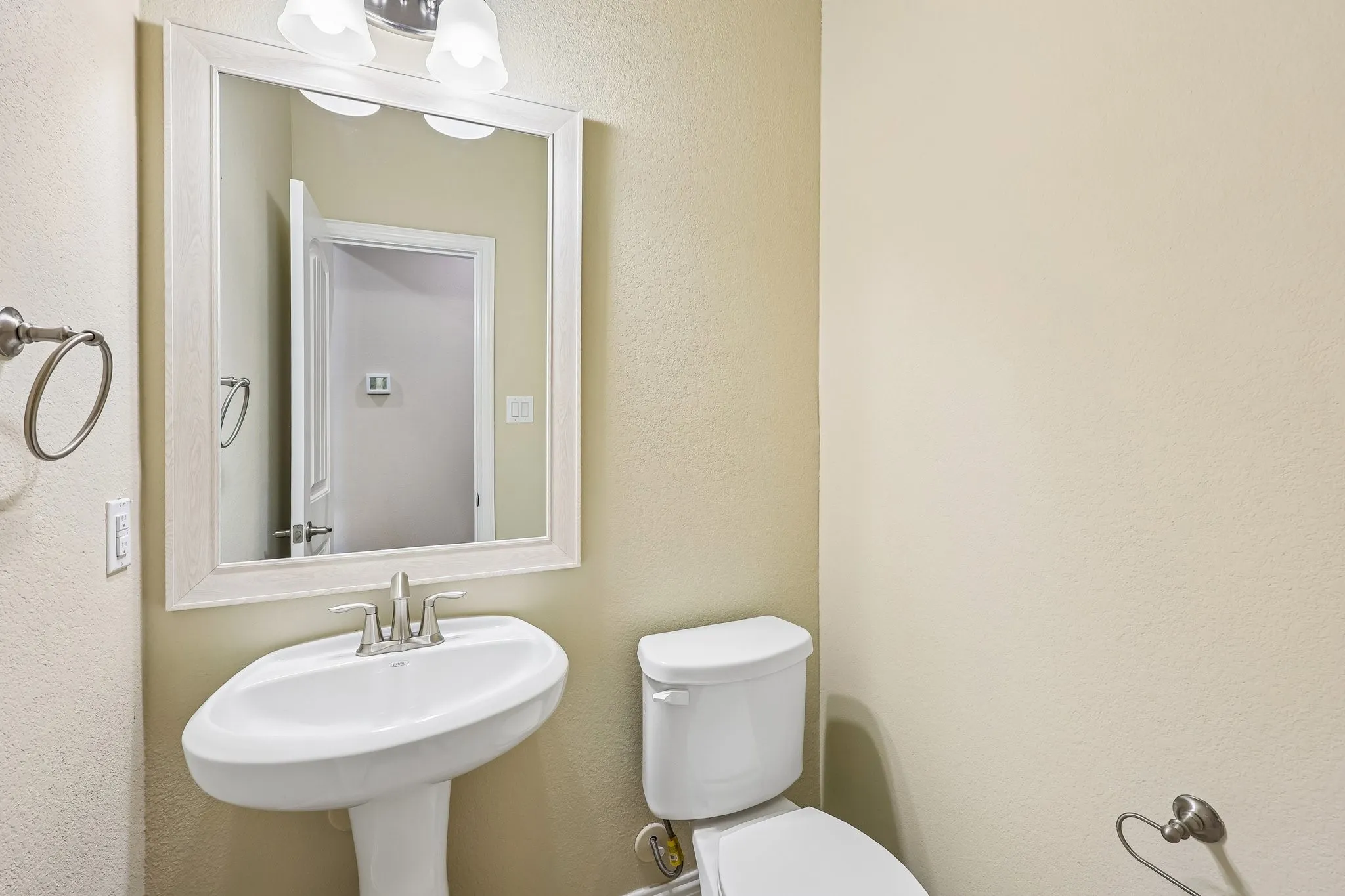 Pedestal sink with chrome faucet, framed mirror, and two-light vanity fixture