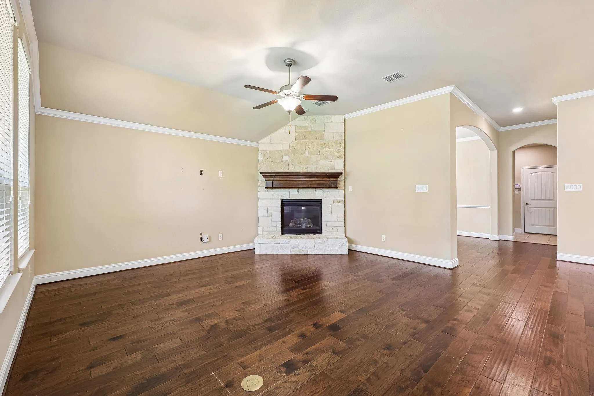 Spacious room featuring rich wood-finish flooring, a corner stone fireplace with a wood mantel, and vaulted ceilings