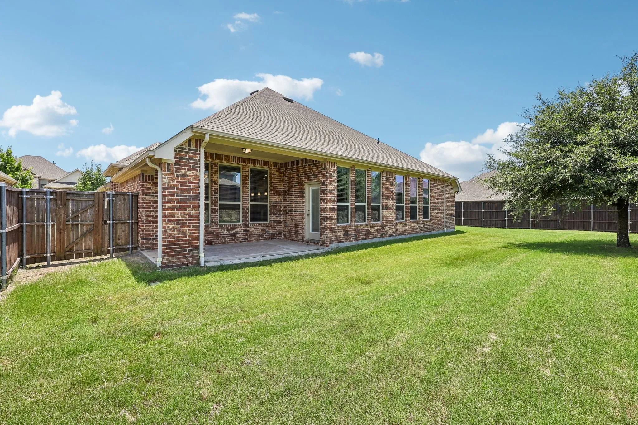 Expansive backyard featuring a brick exterior, covered patio, mature tree, full privacy fencing, and multiple windows