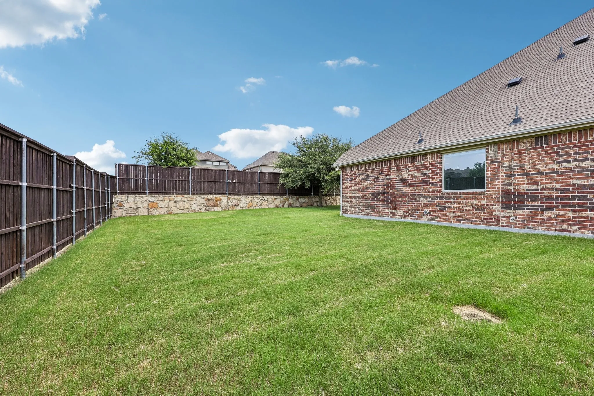 Spacious backyard featuring a manicured lawn, a full privacy fence, and a stone retaining wall