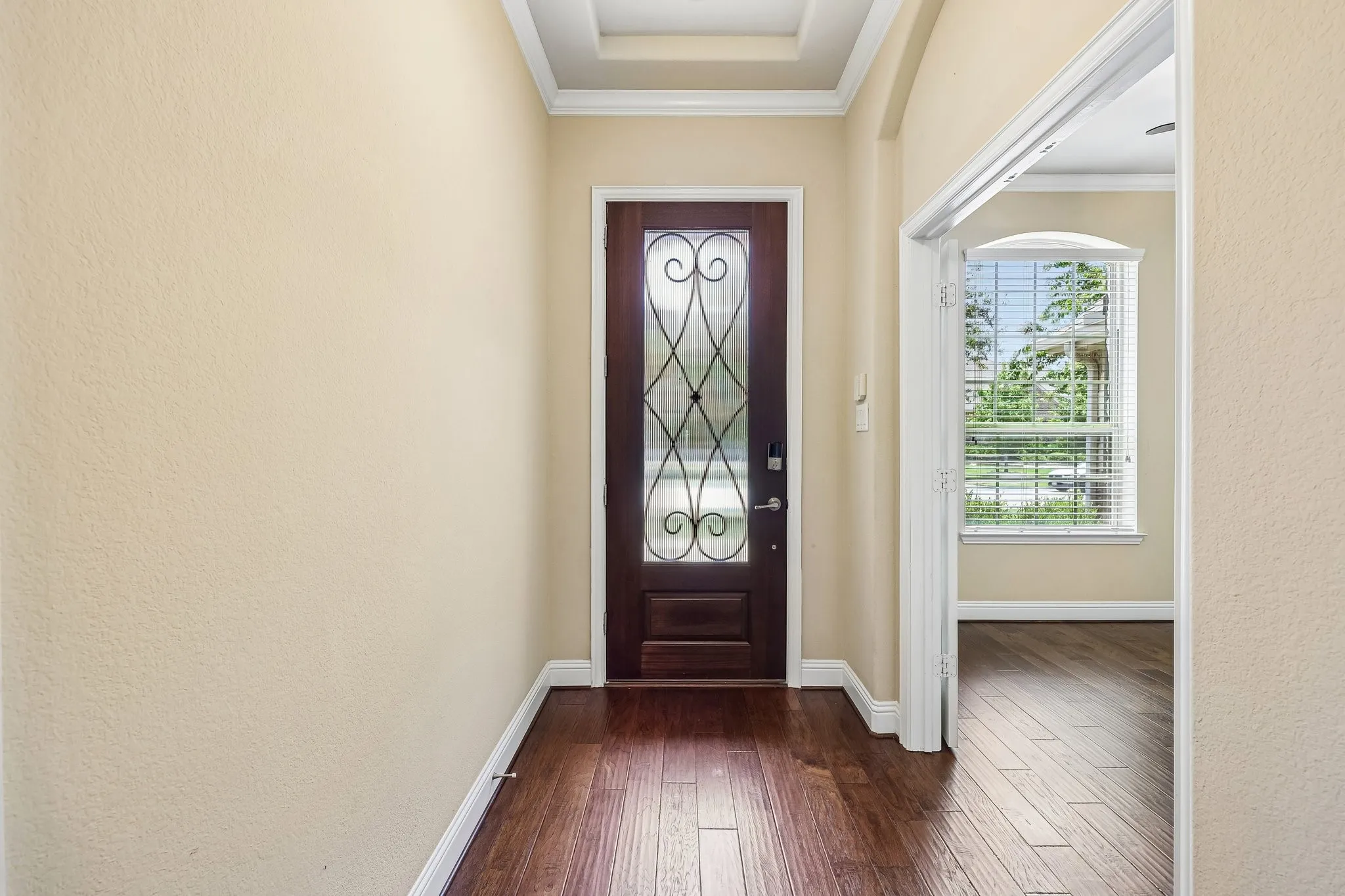 Entryway featuring a dark wood-finish door with decorative glass inlay, crown molding, tray ceiling detail, and rich wood-finish flooring