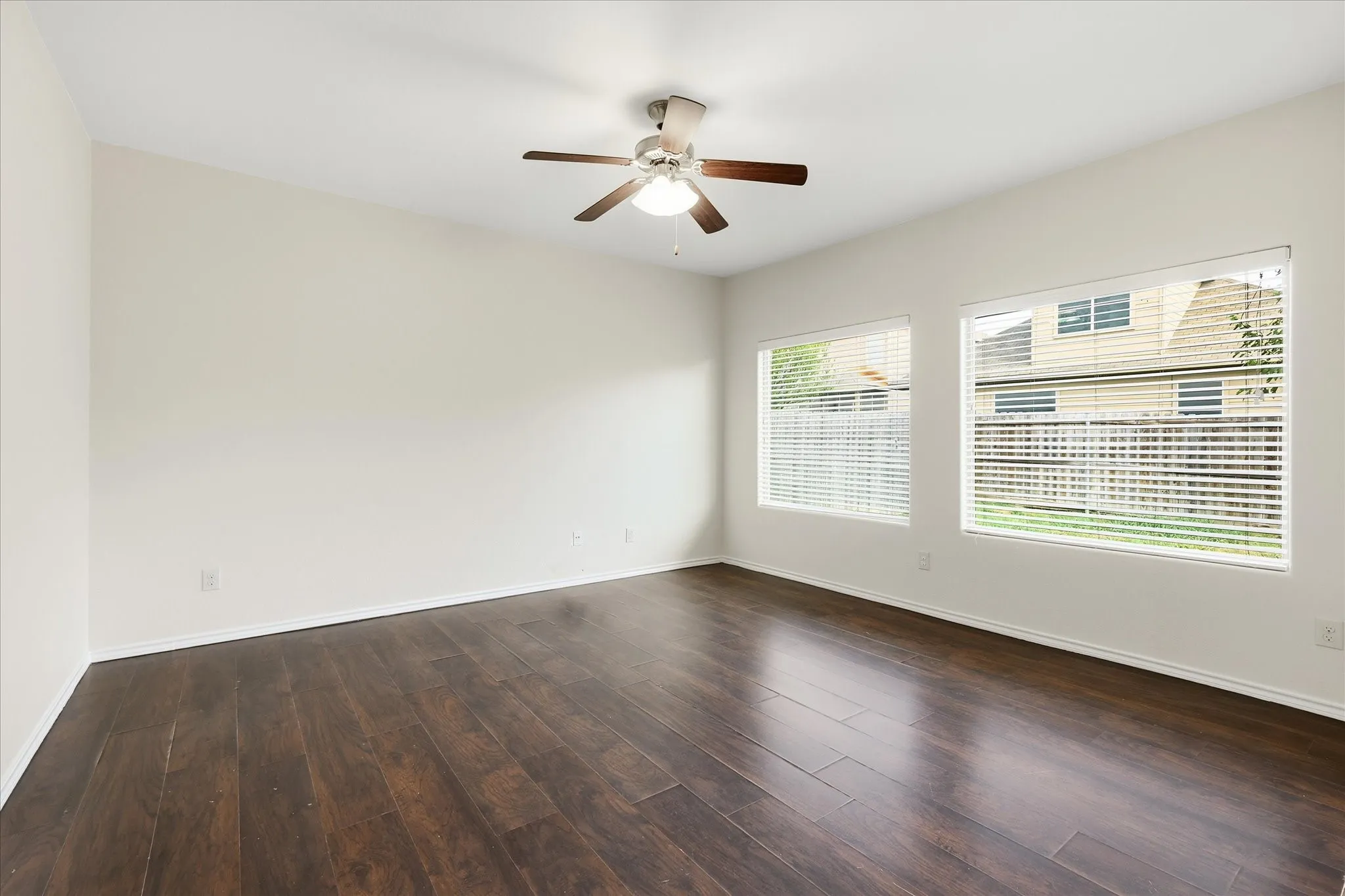 Spacious room featuring dark wood-finish flooring, light-toned walls, and a ceiling fan with integrated lighting