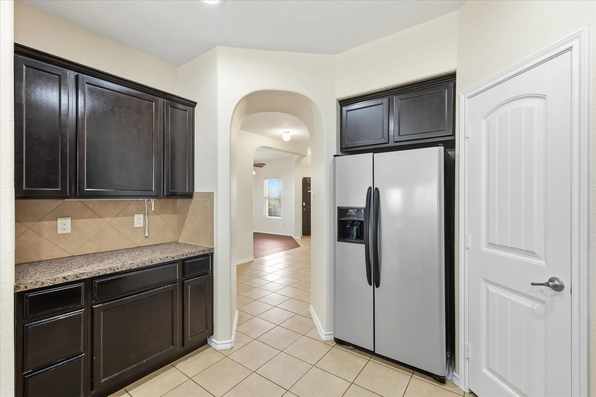 Kitchenette featuring dark wood cabinetry, a light-toned patterned countertop, and a tile backsplash