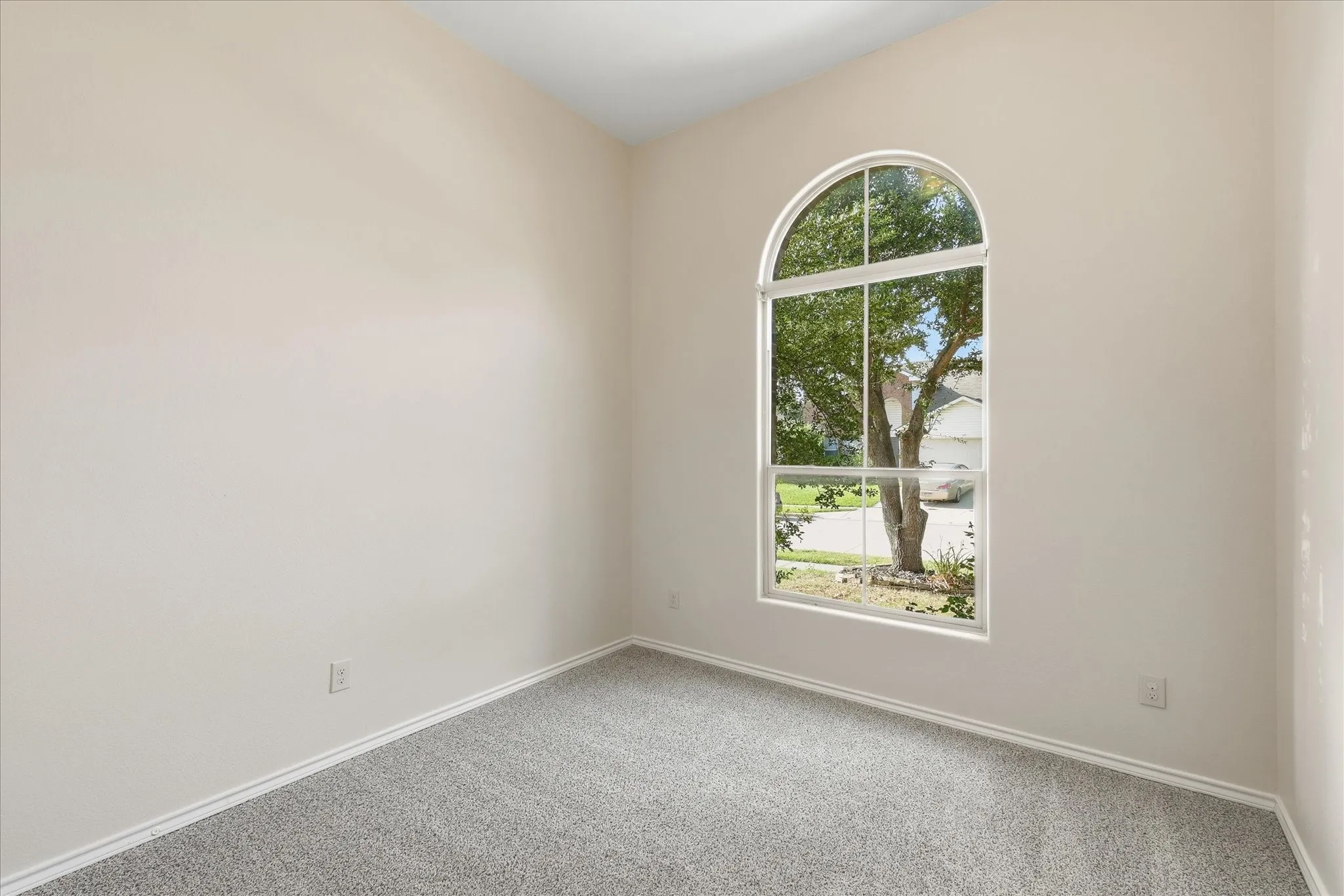 Arched window providing ample natural illumination, neutral wall tones, white trim, and a grey carpeted floor