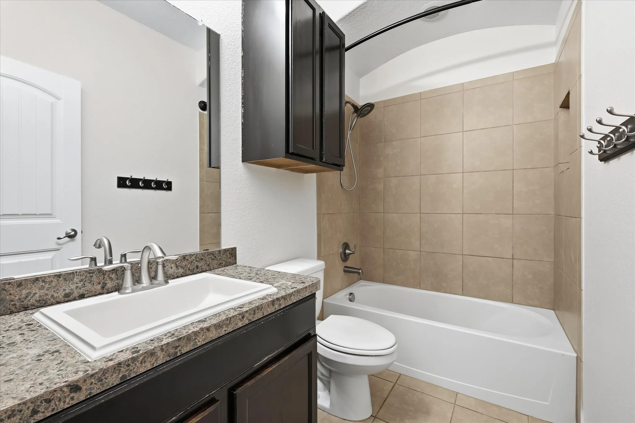 Bathroom featuring a built-in tub with tile surround, a dark wood-finish vanity with an integrated sink, and an overhead medicine cabinet