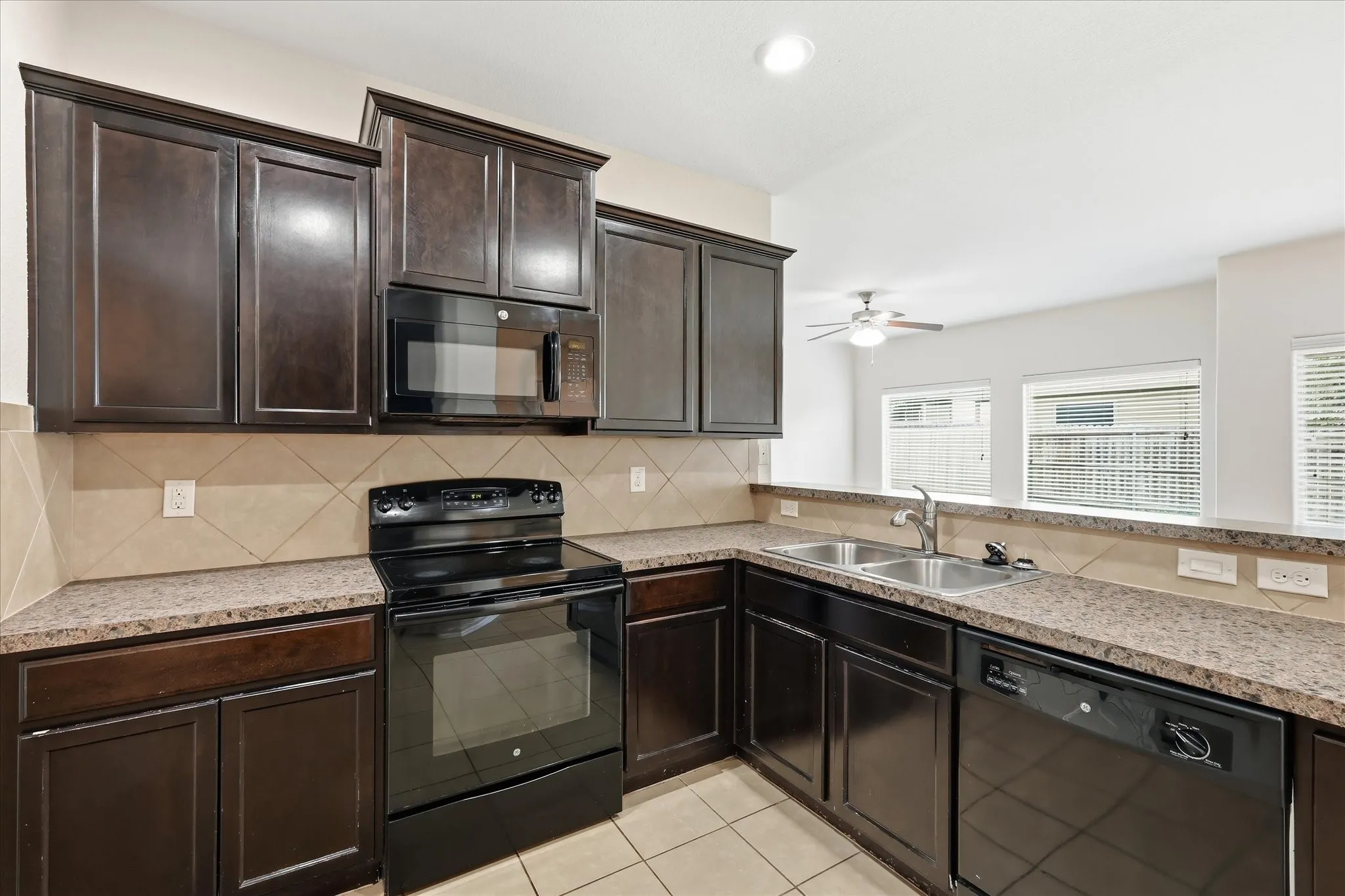 Kitchen featuring dark wood cabinetry, speckled countertops, stainless steel double basin sink, and black appliances including a built-in microwave, electric range, and dishwasher