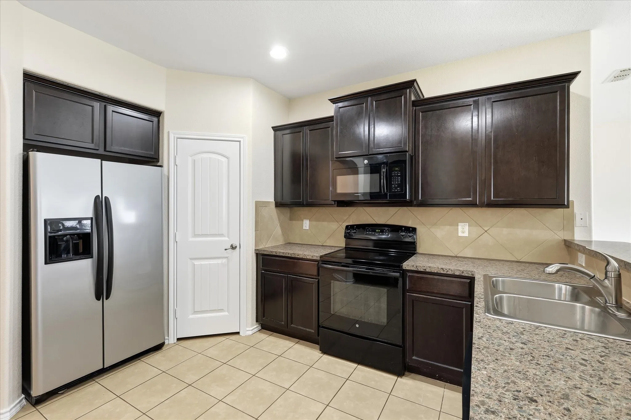 Kitchen featuring dark wood-finish cabinetry, stainless steel side-by-side refrigerator, black electric range with microwave, tile flooring, and laminate countertops