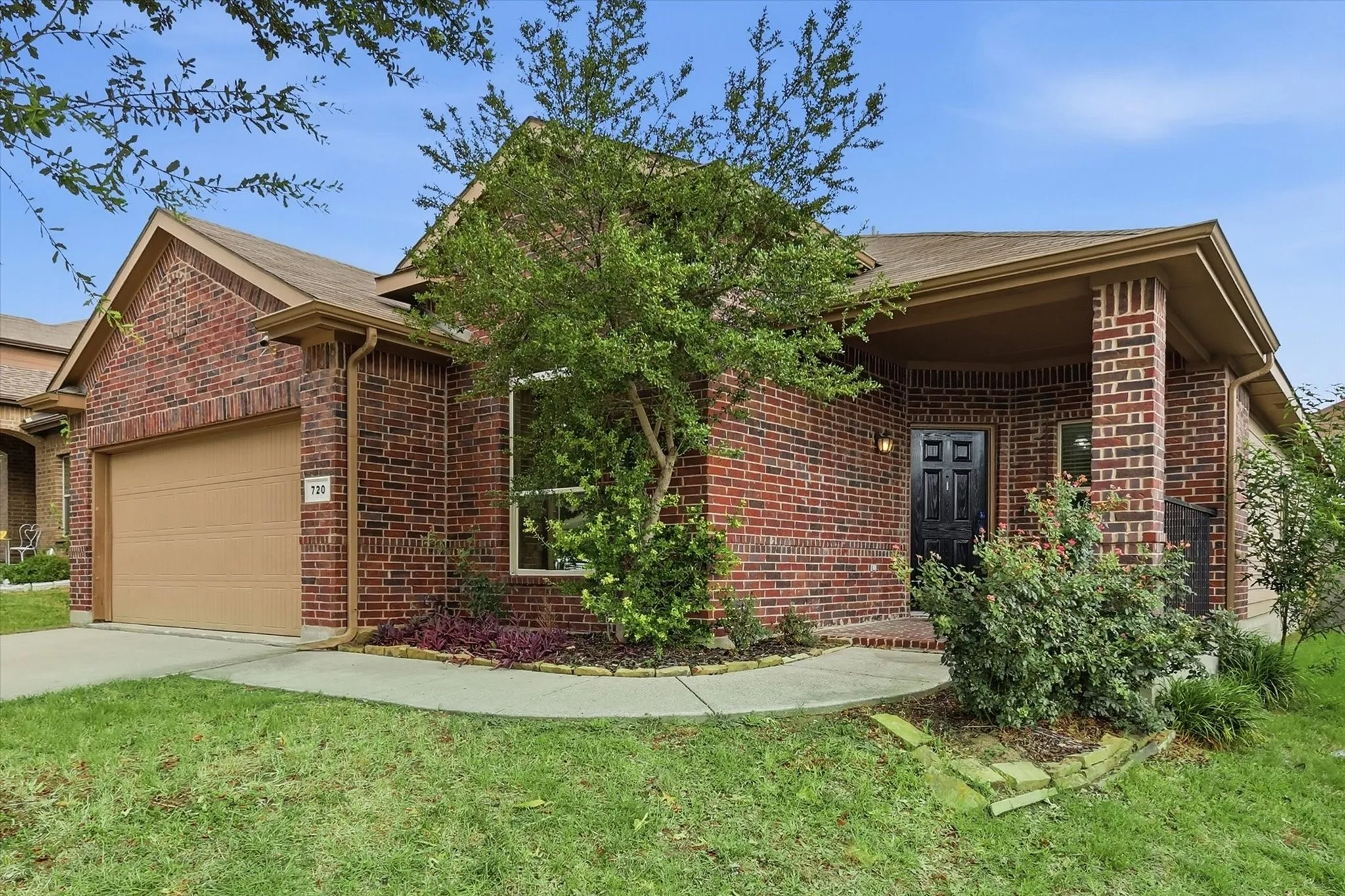 Brick exterior featuring a covered entry, an integrated single-car garage, and a front yard with established landscaping