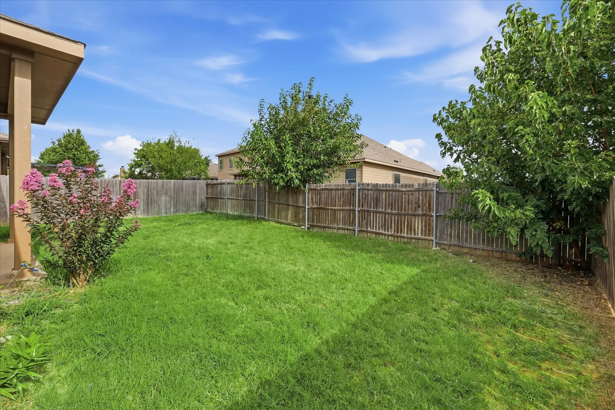 Expansive backyard featuring a lush lawn, mature trees, a flowering shrub, and a wooden privacy fence