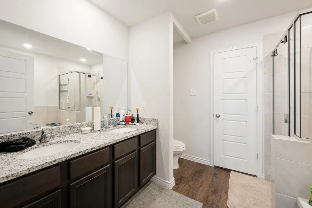 Bathroom featuring a dual-sink vanity with granite countertops, rich wood-finish cabinetry, and a large frameless mirror