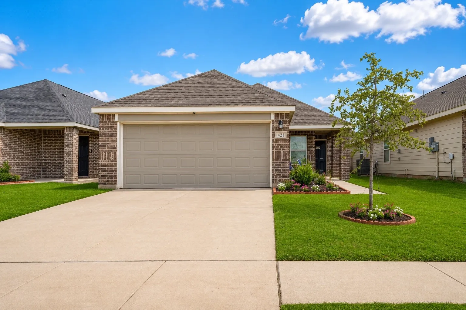 Brick facade home featuring a two-car garage, mature landscaping, and a concrete driveway
