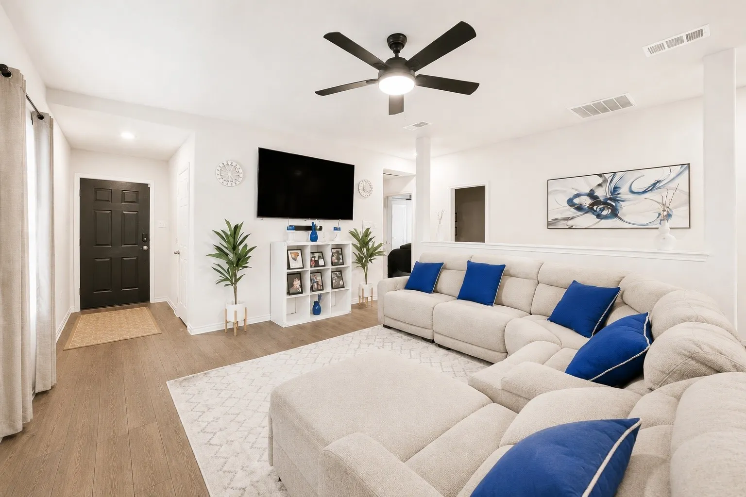 Open-concept living area featuring wood-finish flooring, recessed lighting, a ceiling fan with integrated light, and a black paneled entry door
