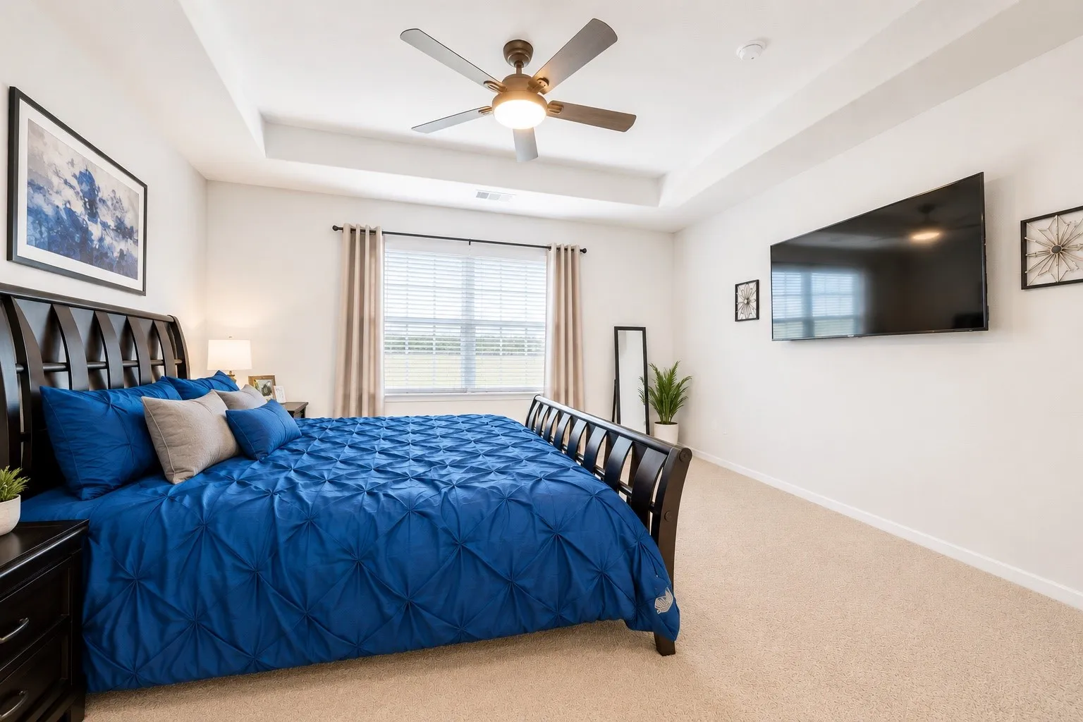 Spacious room featuring a tray ceiling, ceiling fan with integrated lighting, light-toned carpeting, and a window with blinds and drapes