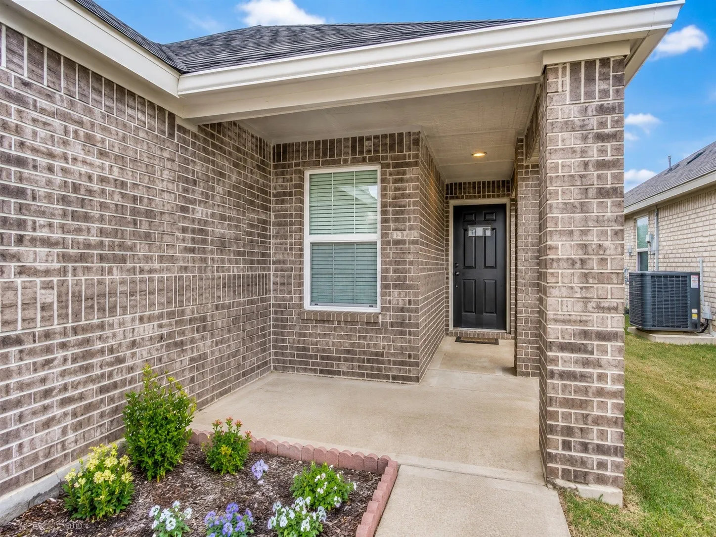 Covered entryway featuring a dark brick facade and a solid black entry door with decorative glass inserts