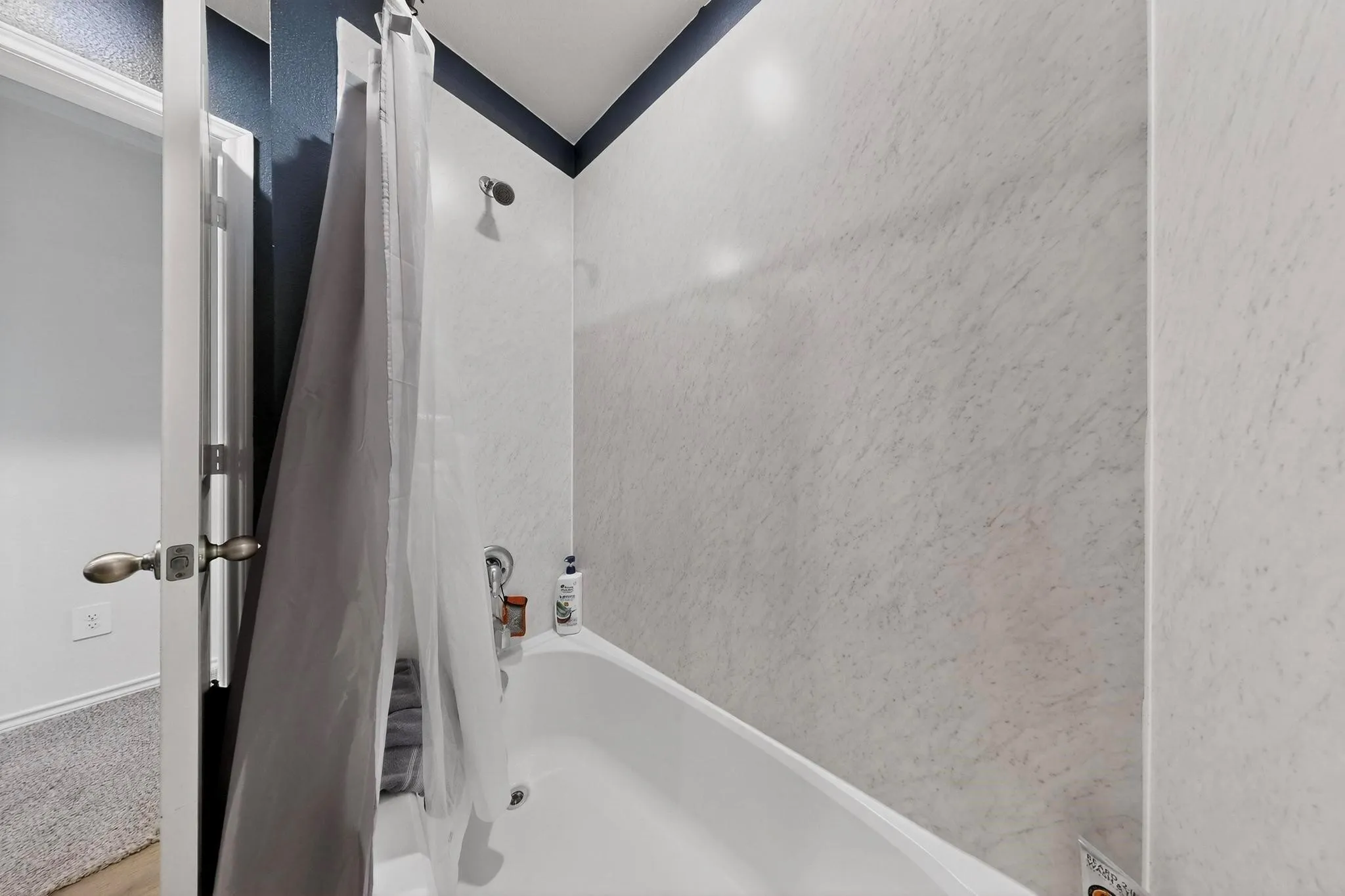 Bathtub with a shower enclosure featuring a white surround and a wall-mounted showerhead