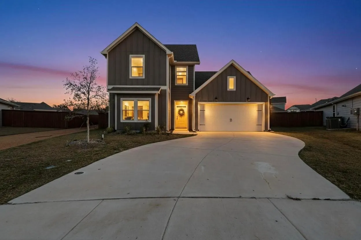Contemporary two-story residence featuring dark siding, a light-colored front door, and a two-car garage