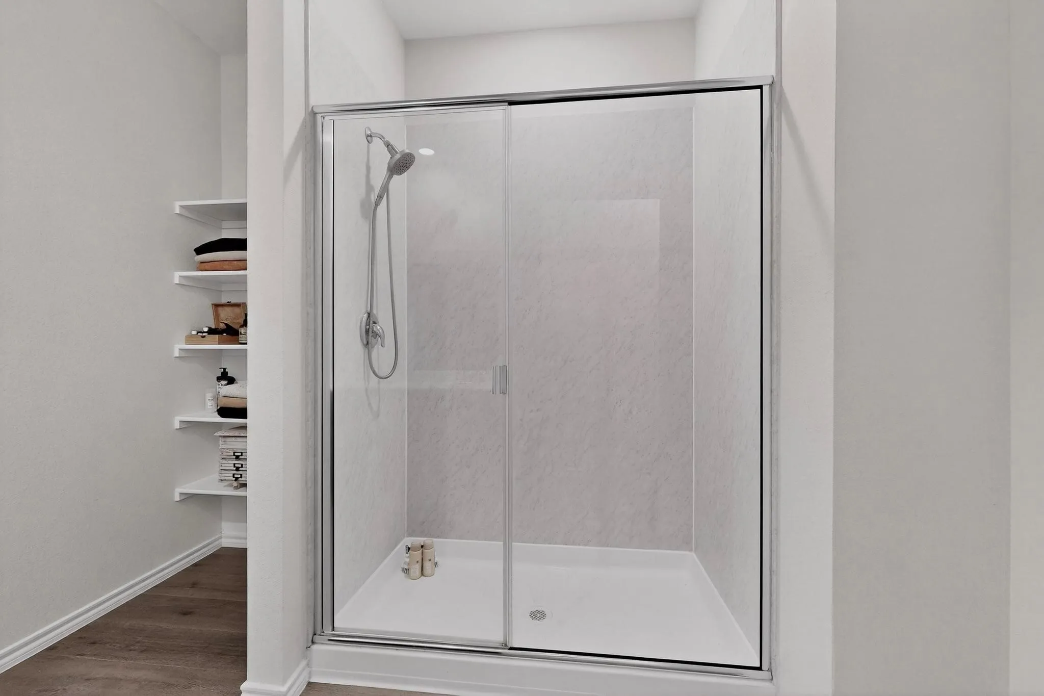 Shower enclosure with sliding glass door, white shower base, and integrated shower head
