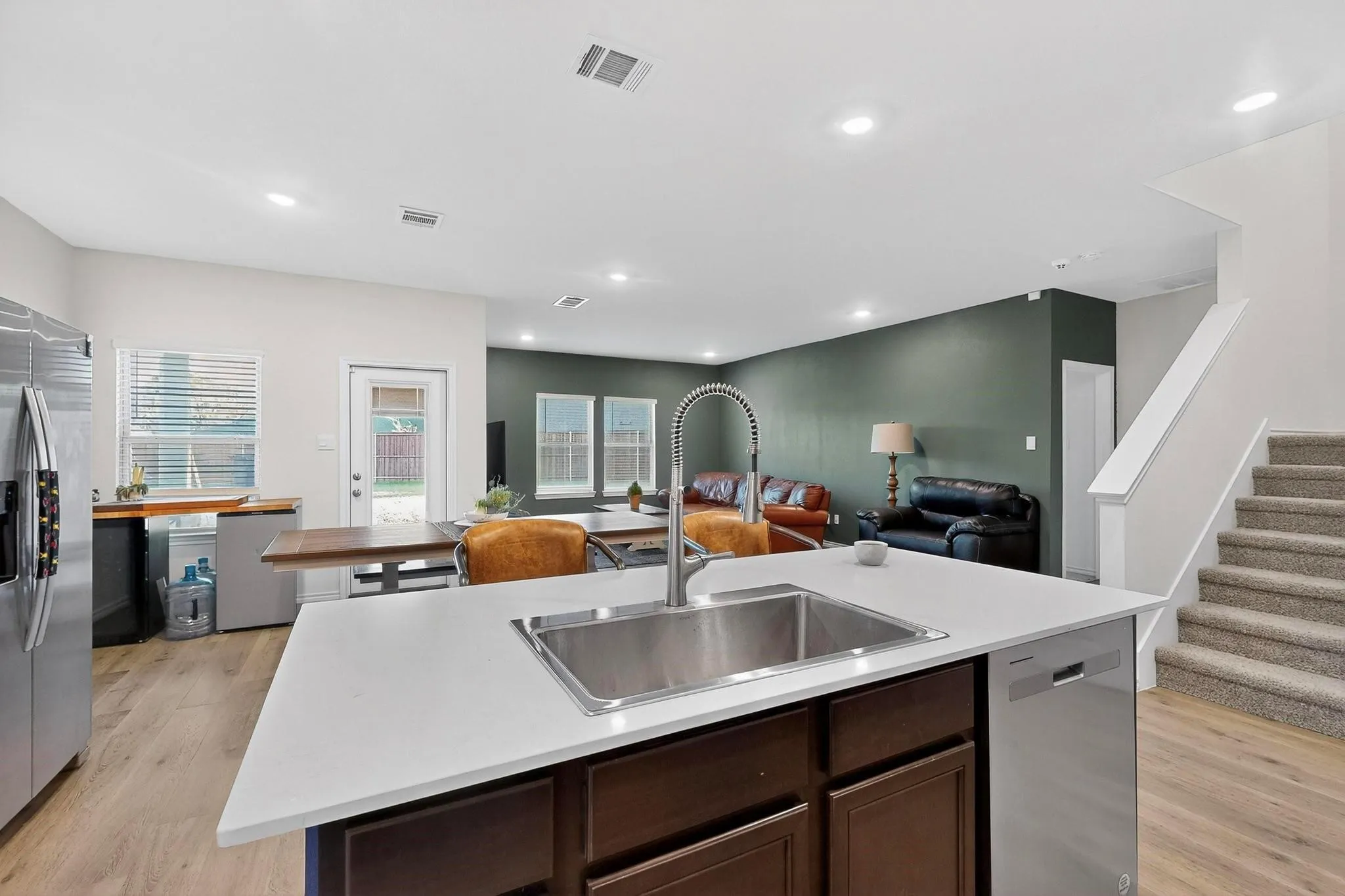 Kitchen island featuring an undermount sink with a gooseneck faucet, light-toned countertop, and integrated dishwasher
