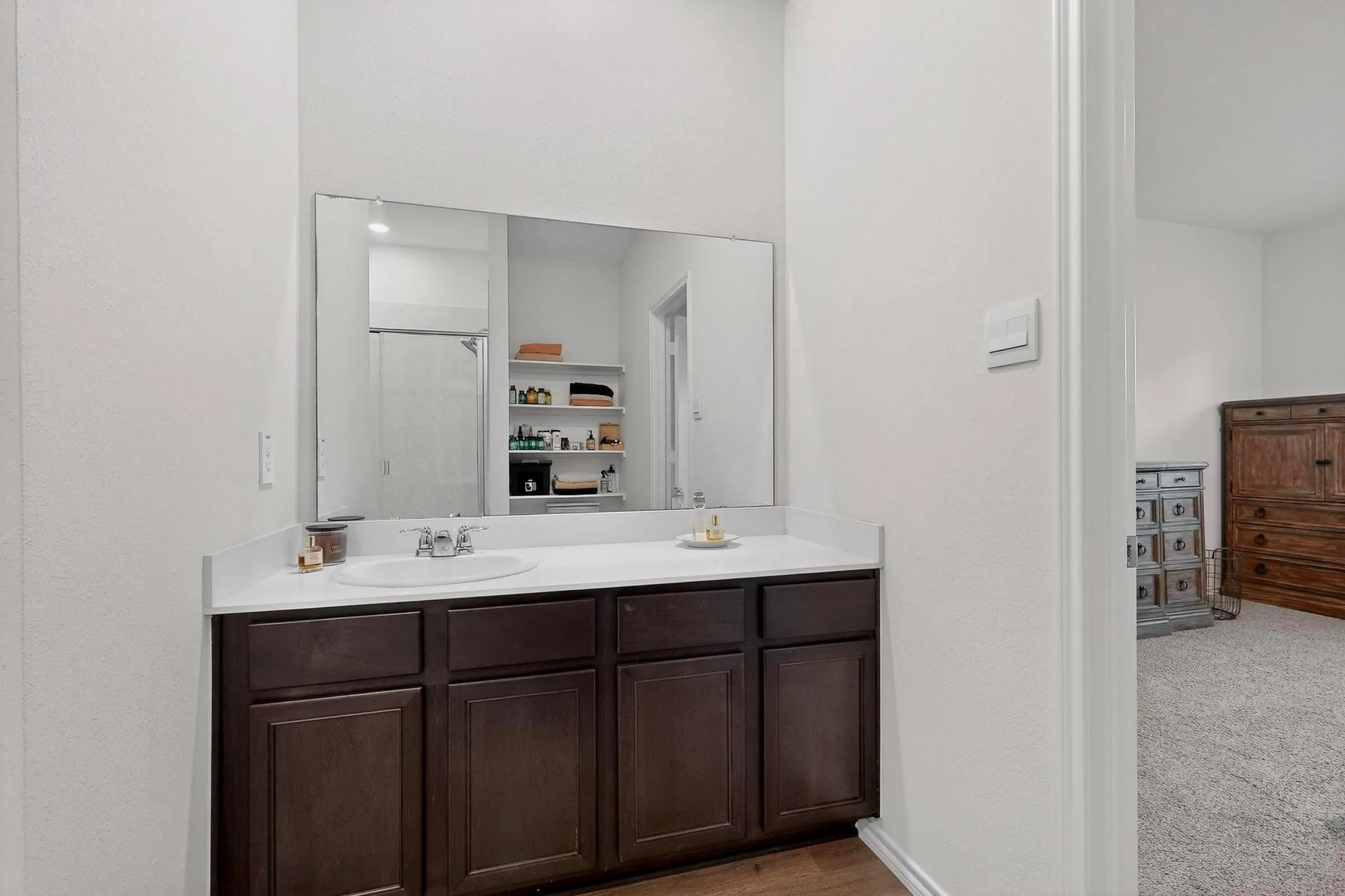 Bathroom vanity featuring a single basin sink set into a light-colored countertop, dark wood-finish cabinetry, and a large wall-mounted mirror