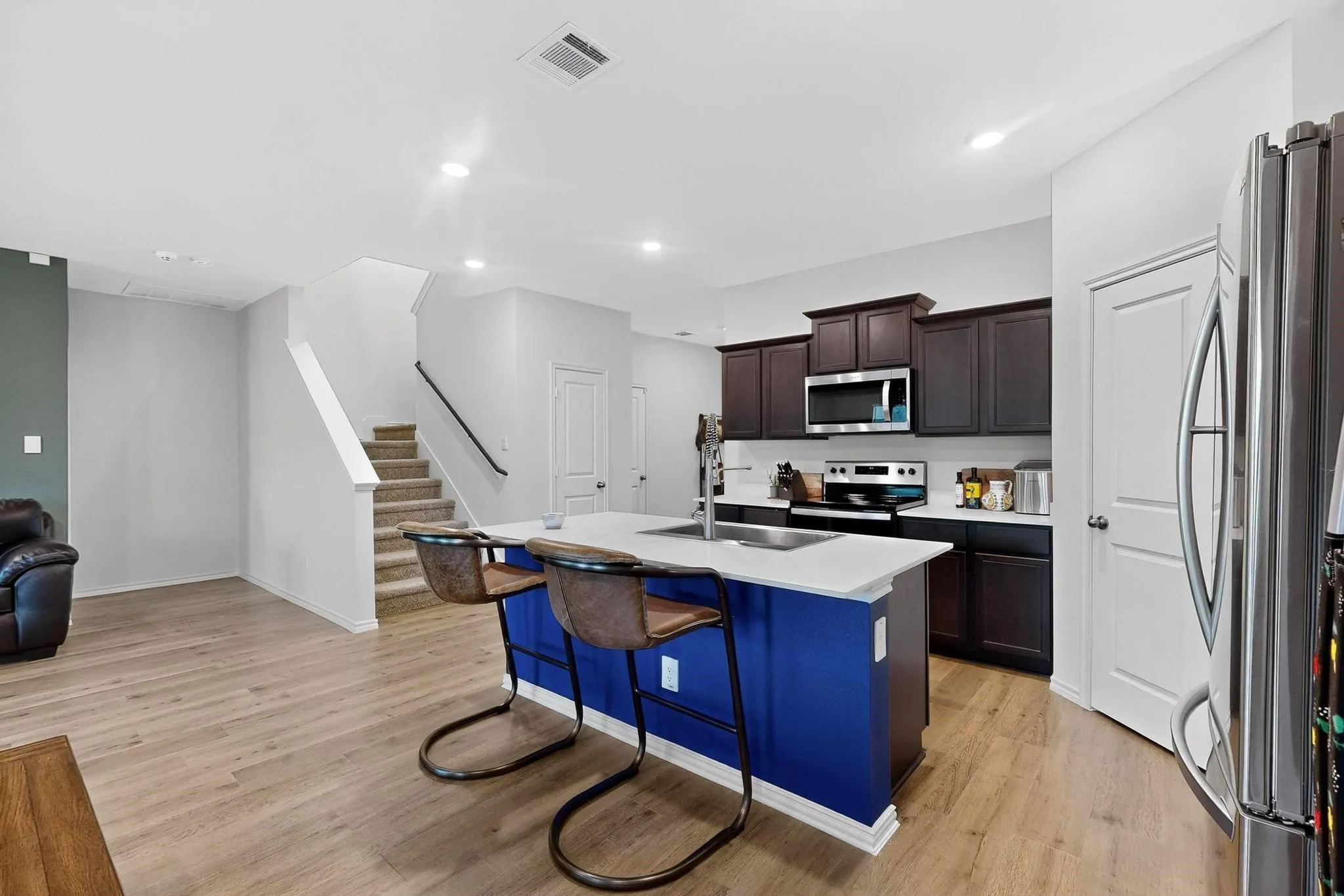 Kitchen featuring a bright blue island with seating, white countertop, stainless steel sink, and dark wood-finish cabinetry
