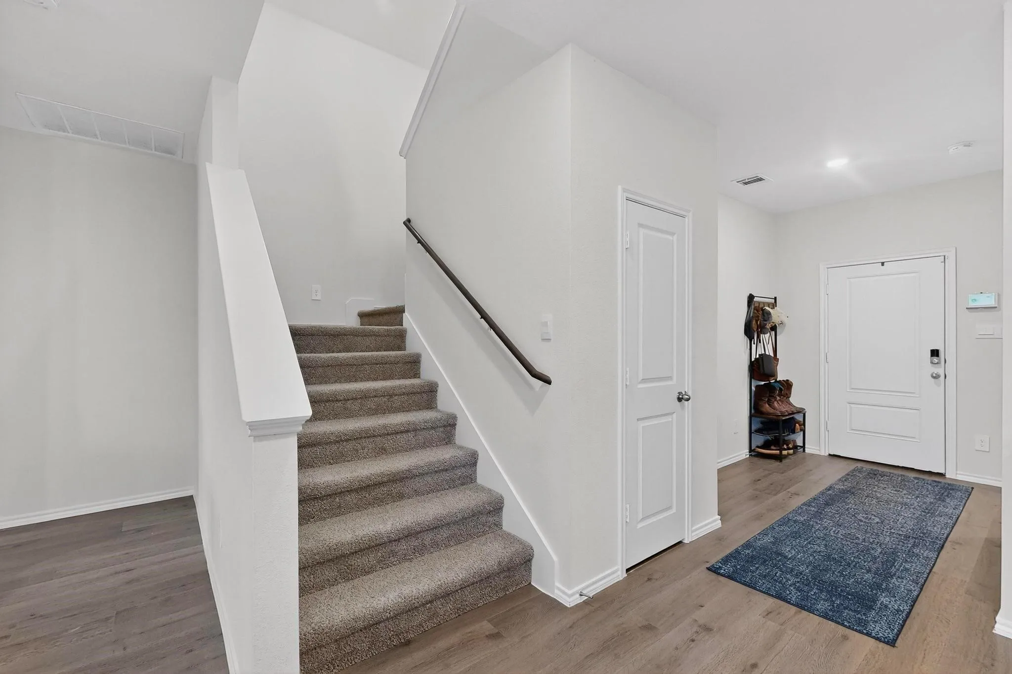 Carpeted staircase with black handrail, wood-finish flooring, white paneled doors, and recessed lighting