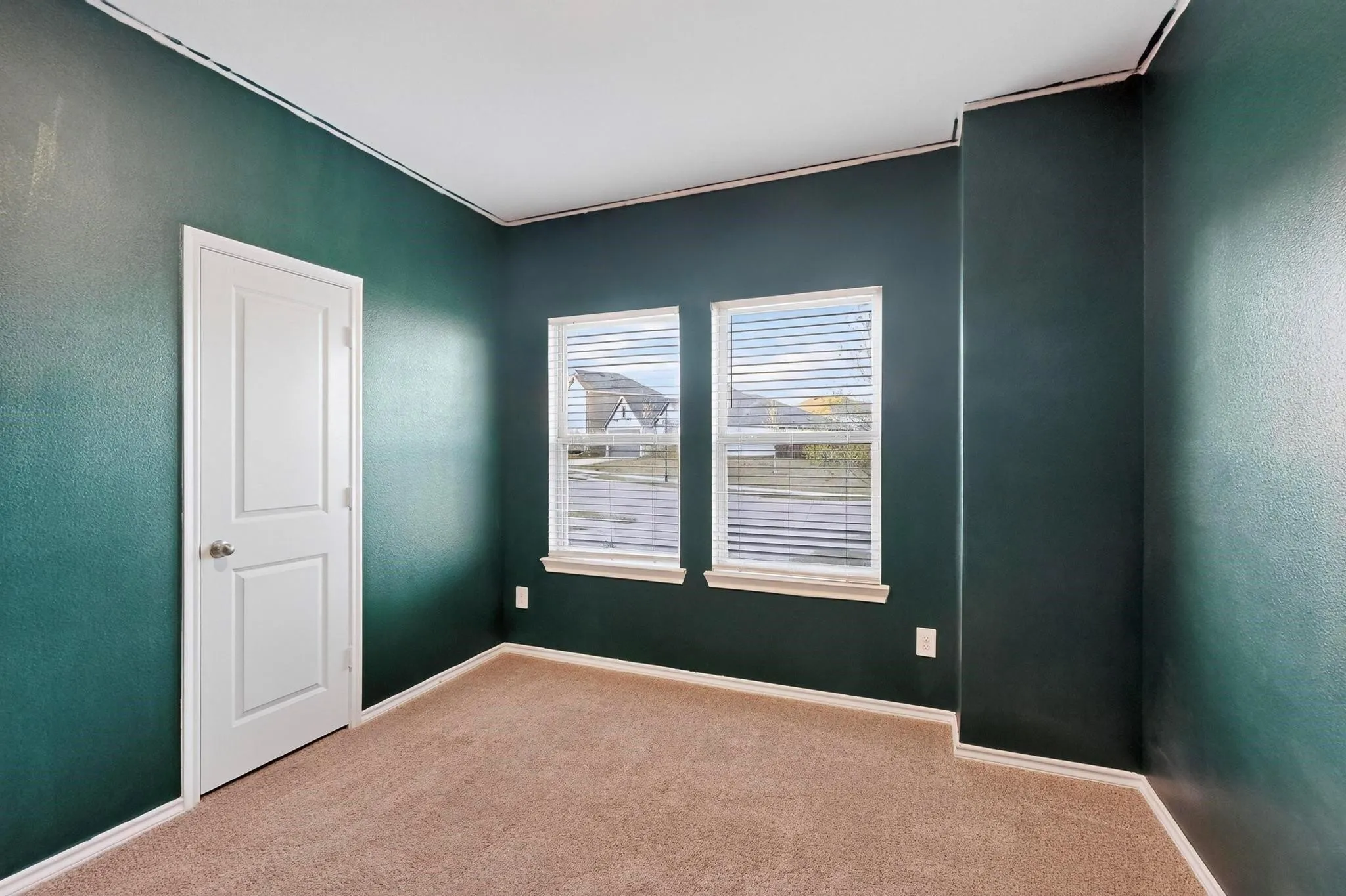 Room featuring two windows with horizontal blinds, contrasting trim, and carpet flooring