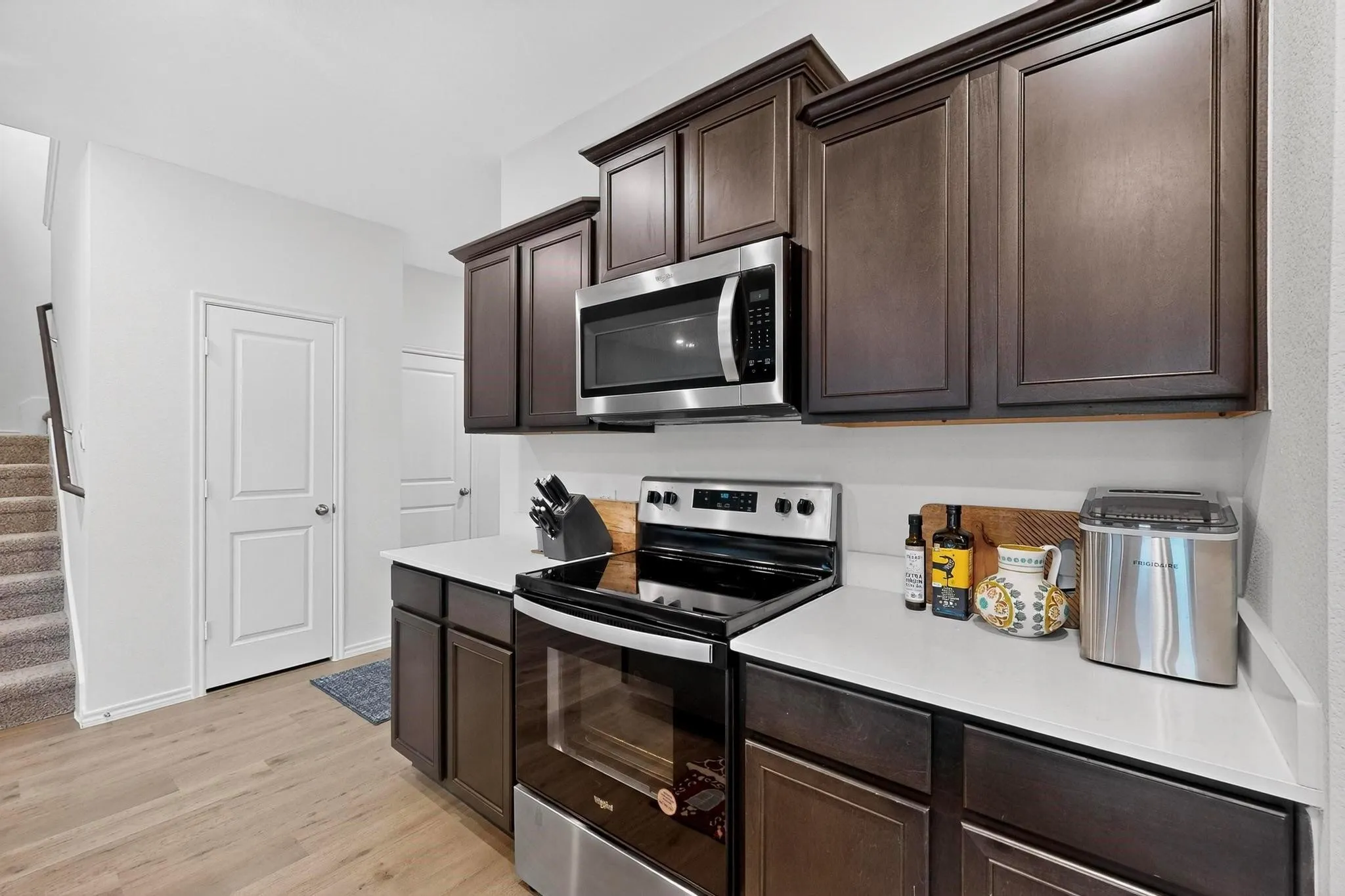 Kitchen featuring wood-finish flooring, dark wood cabinetry, white countertops, and stainless steel appliances including a range and microwave