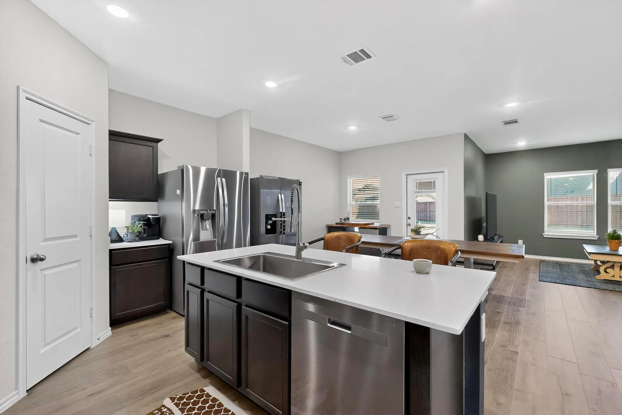 Open-concept kitchen featuring an island with an undermount sink, stainless steel appliances, dark wood cabinetry, light countertops, and wood-finish flooring