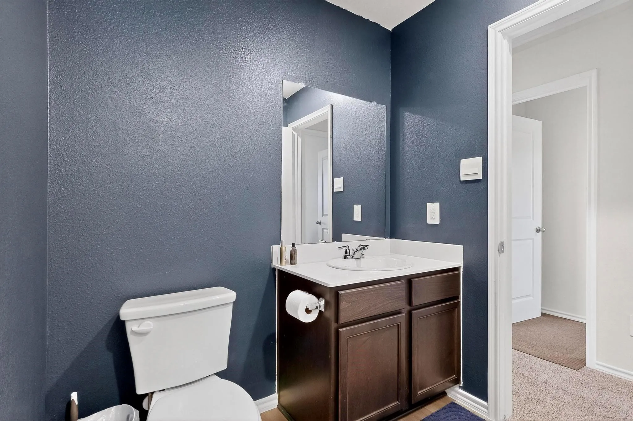 Bathroom vanity featuring a white countertop with an integrated sink, dark wood-finish cabinetry, and a wall-mounted mirror