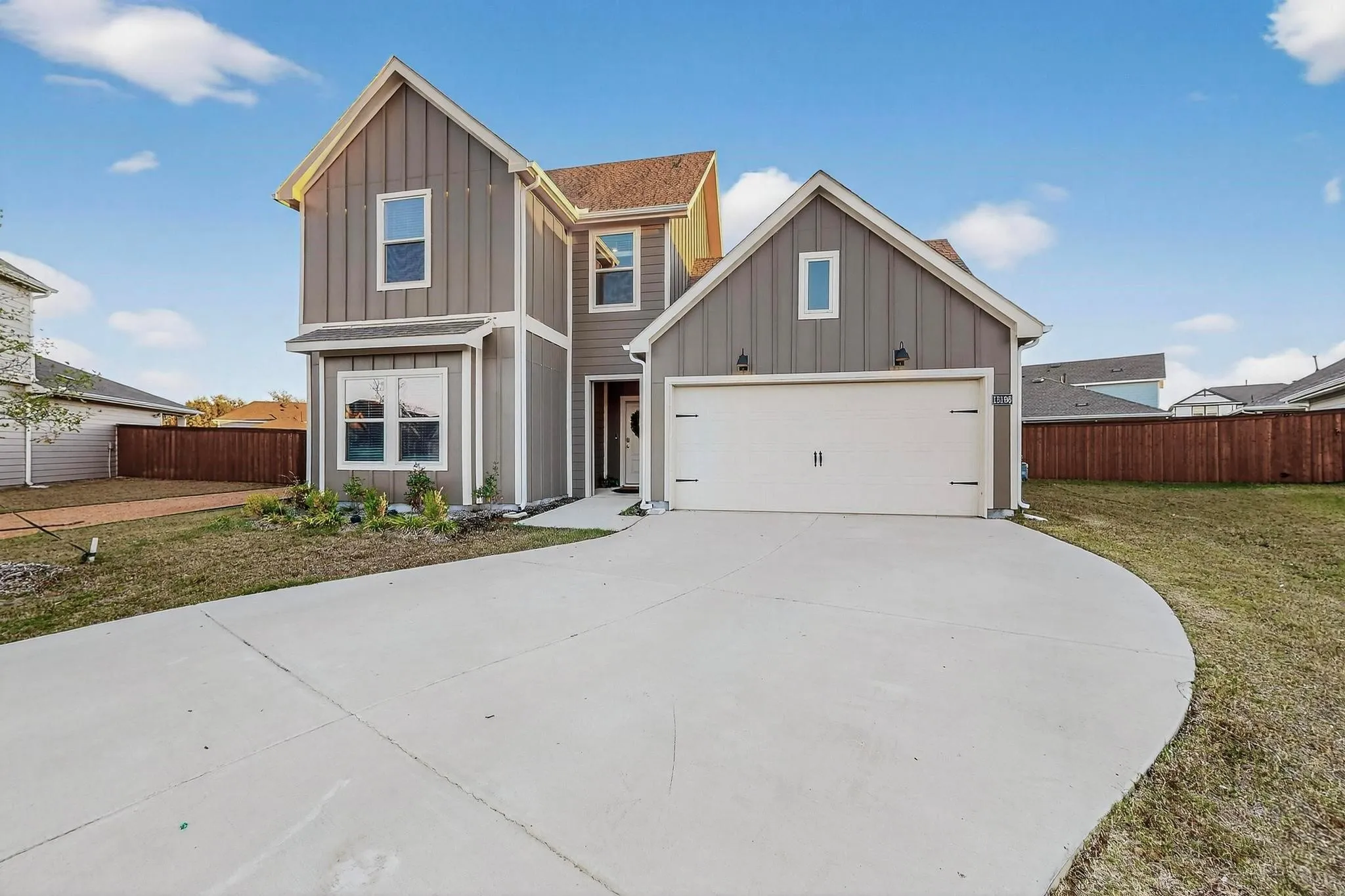 Contemporary two-story residence featuring board and batten siding, a prominent two-car garage, and a concrete driveway