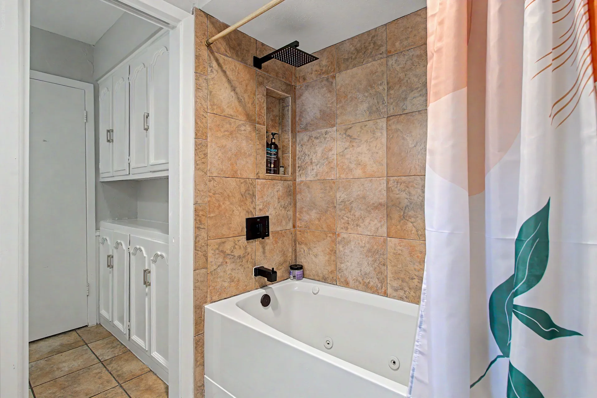 Bathroom featuring a jetted tub, tiled surround with a shower niche, matte black fixtures, and built-in white cabinetry