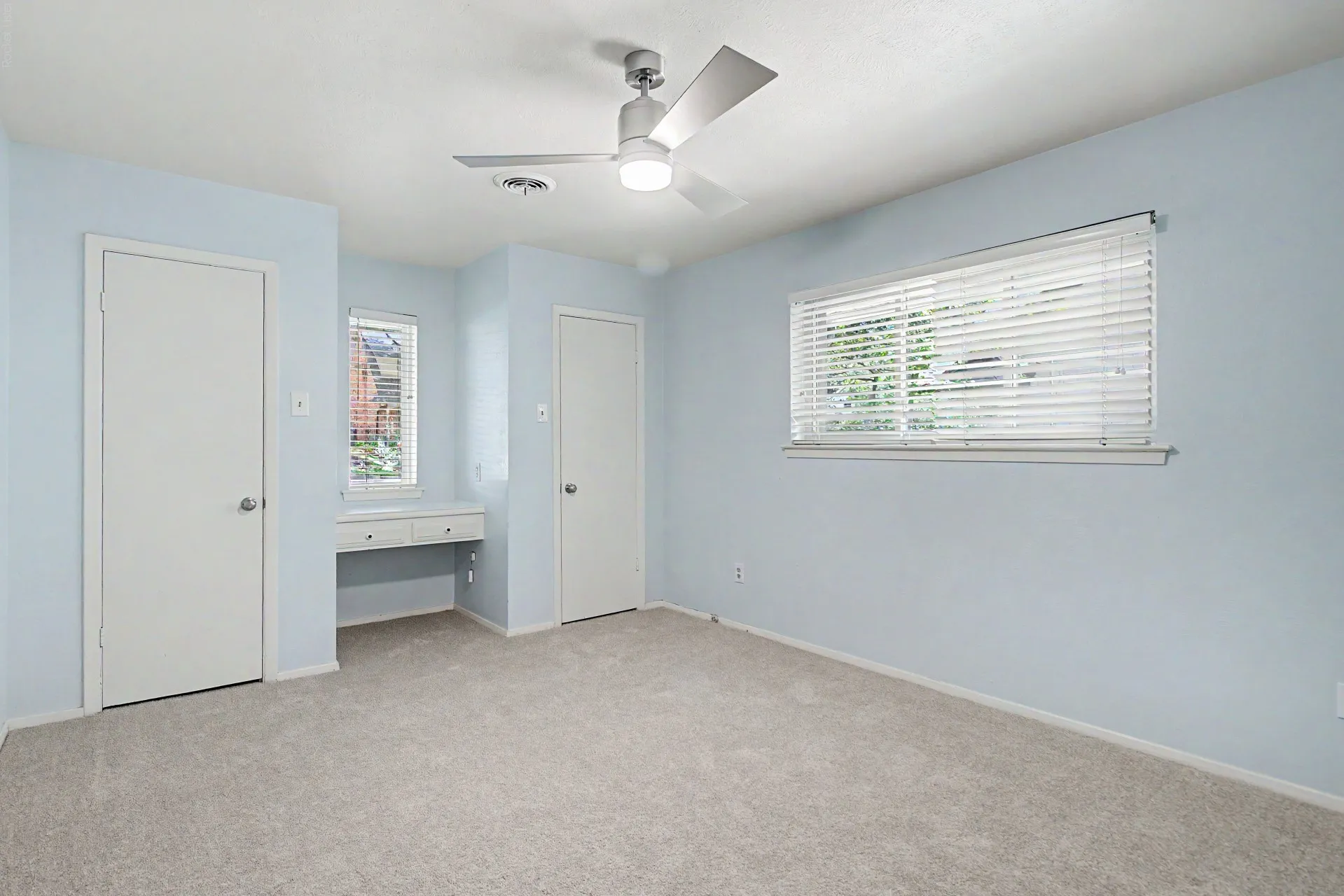 Carpeted room featuring a ceiling fan with integrated lighting, two white doors, and multiple windows with blinds