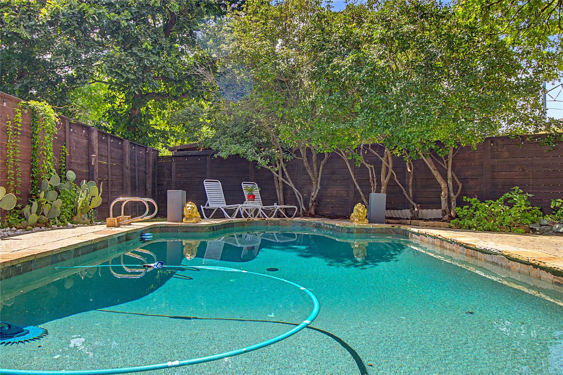 In-ground swimming pool with flagstone coping, surrounded by mature trees and a privacy fence