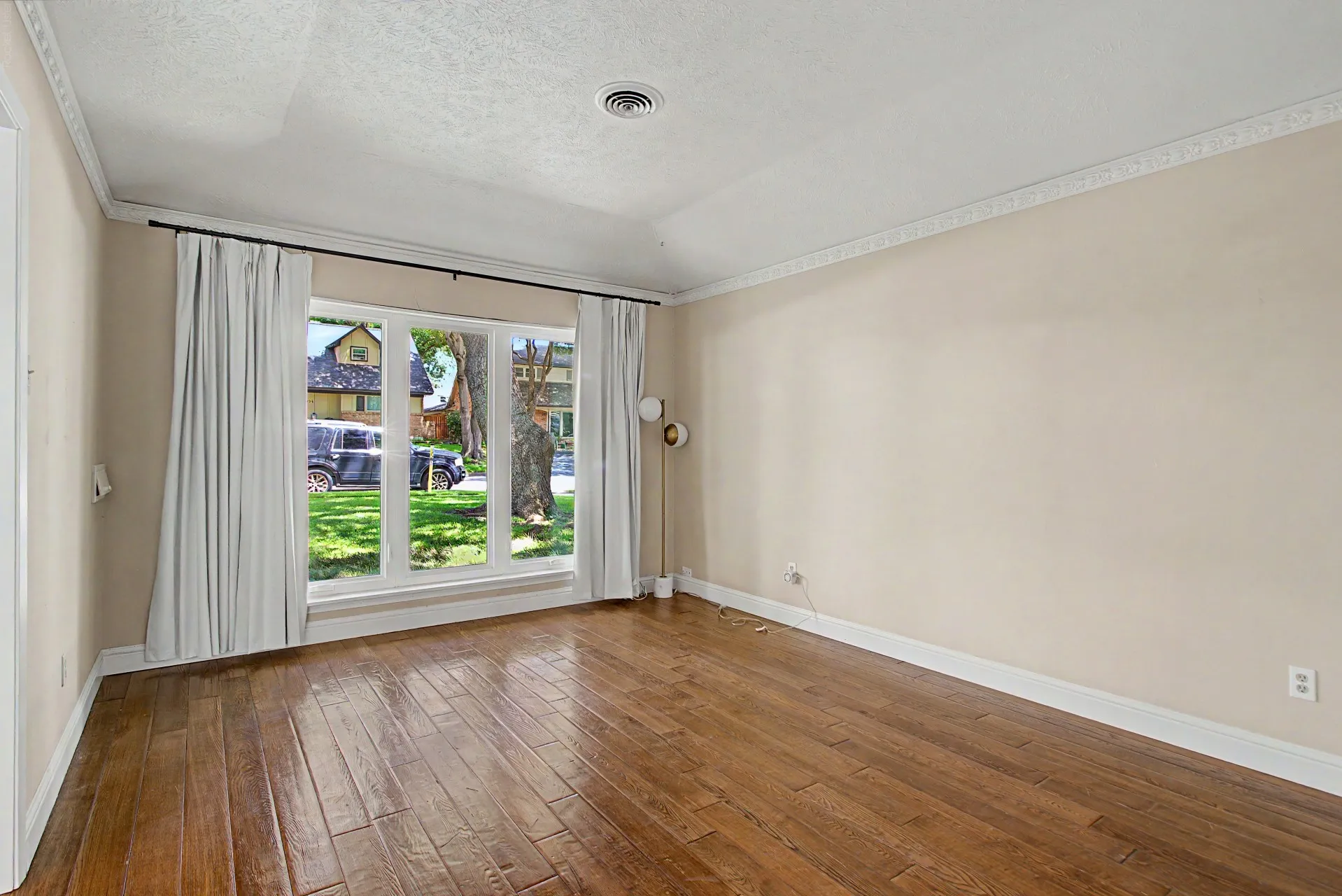 Spacious room featuring wood-finish flooring, a large multi-pane window, crown molding, and neutral wall tones