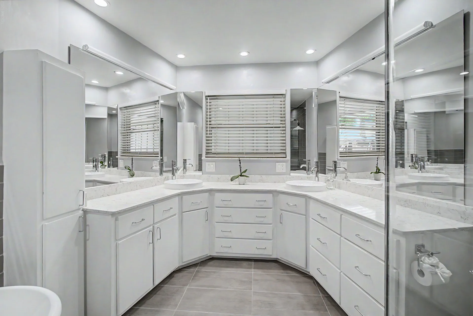 Dual vessel sinks set into a curved vanity with white cabinetry and light-colored countertops