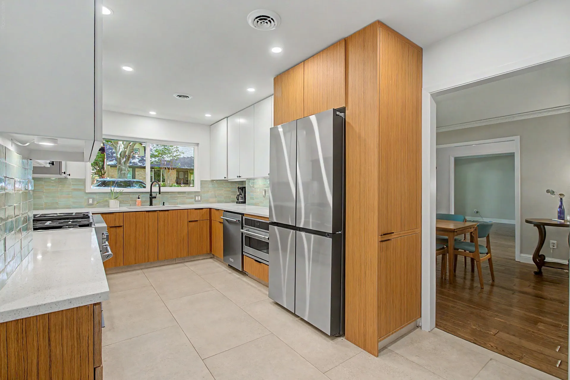Modern kitchen featuring white and wood-finish cabinetry, stainless steel appliances, light-toned tile flooring, light-colored countertops, and a full-height tile backsplash